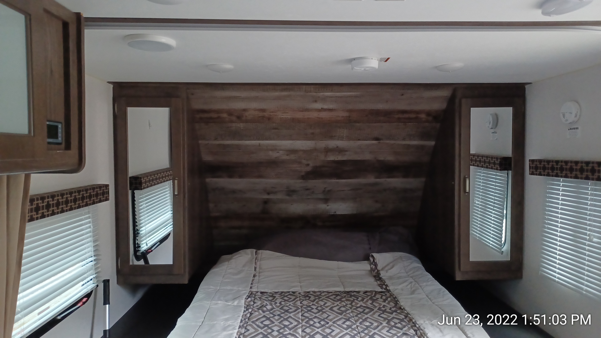 Cozy RV rental bedroom showing a bed, rustic wood headboard, and mirrored side wardrobes.. Keystone RV Passport Express 2019
