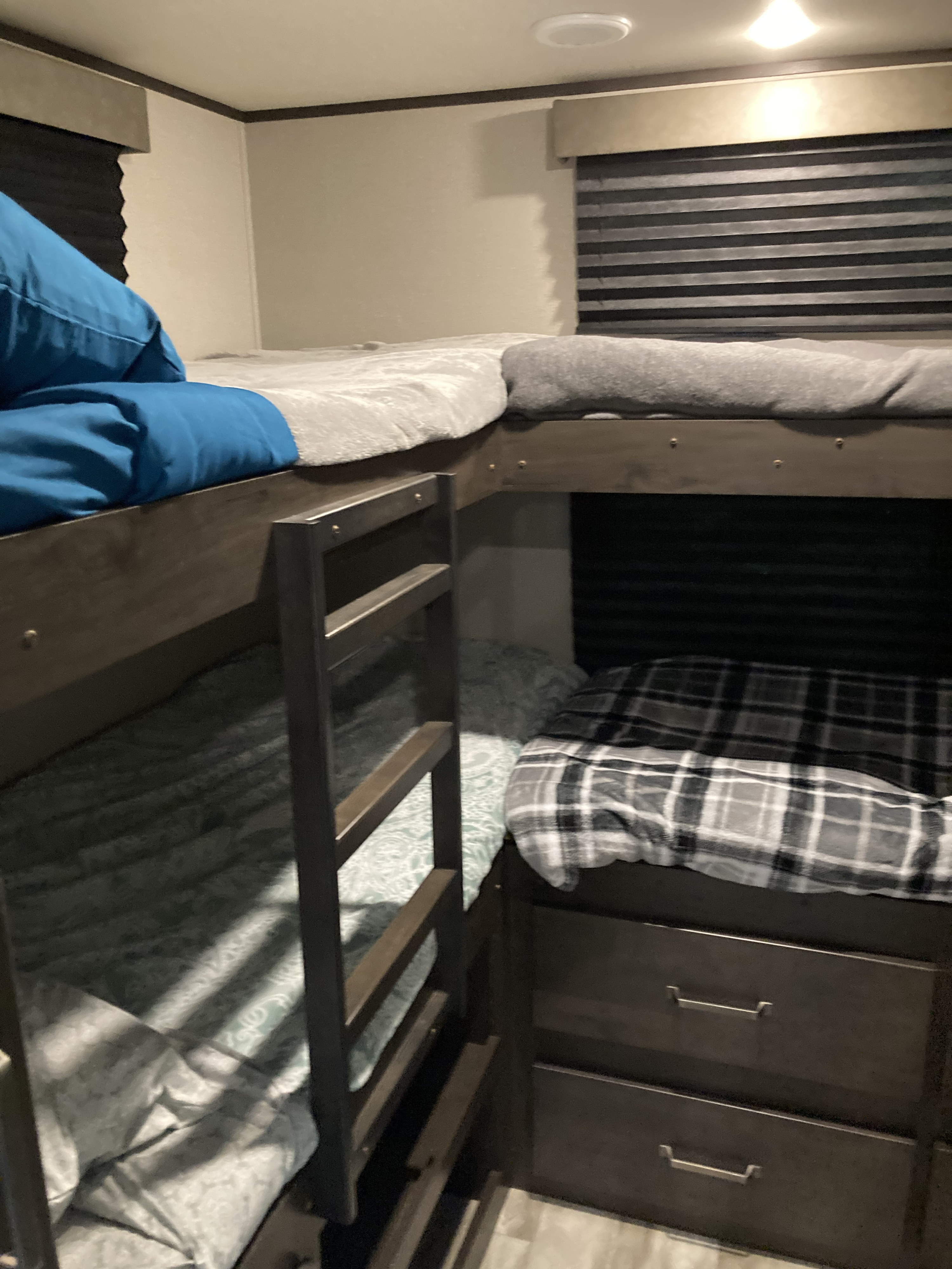 Cozy RV rental bunk beds feature blue and plaid bedding, dark wood frames, and practical storage drawers, ideal for travel.. Grand Design Transcend 2021