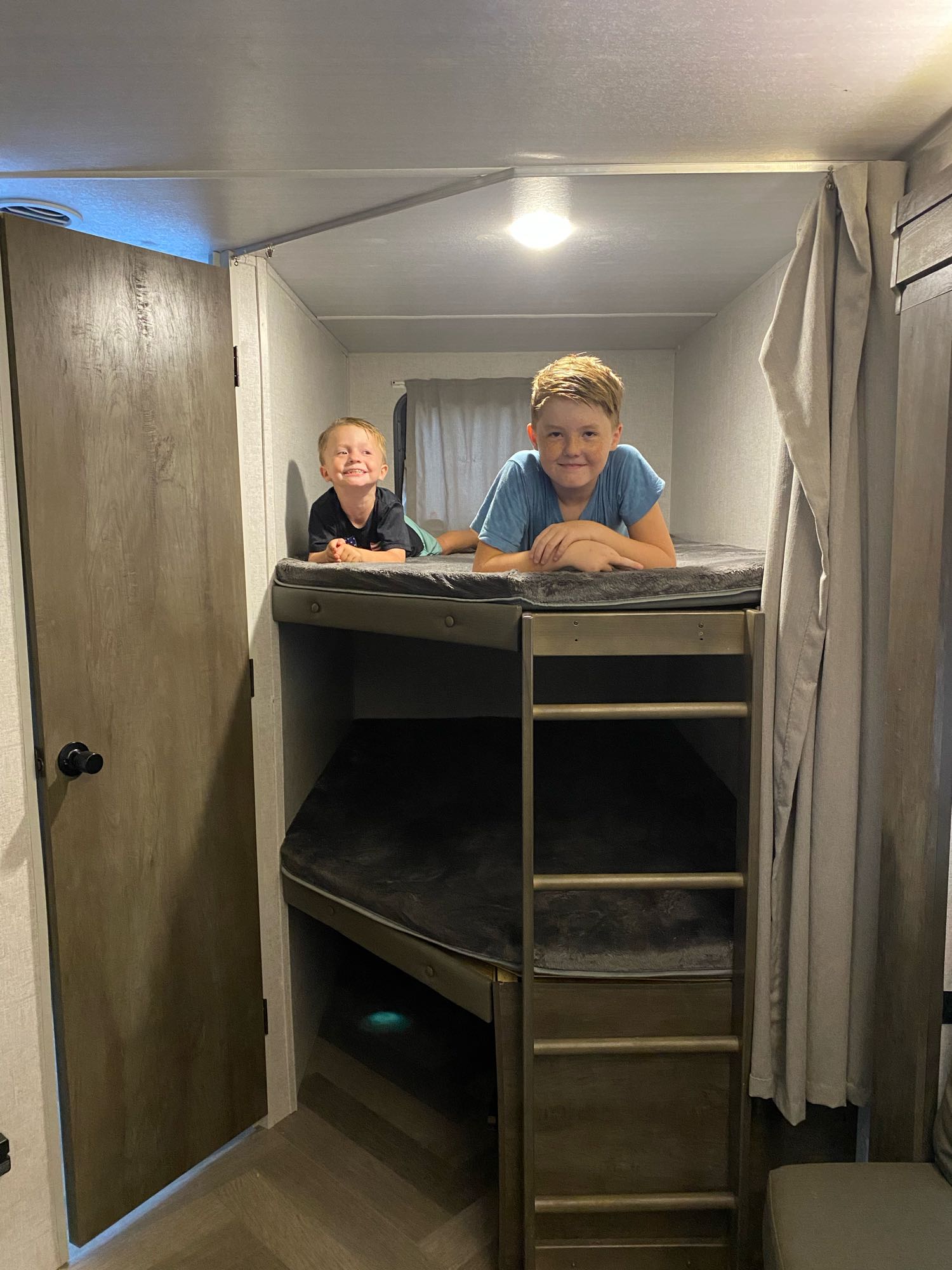 Two happy boys in an RV rental, enjoying their bunk beds. A cozy space for family trips.. Forest River Wildwood 2021