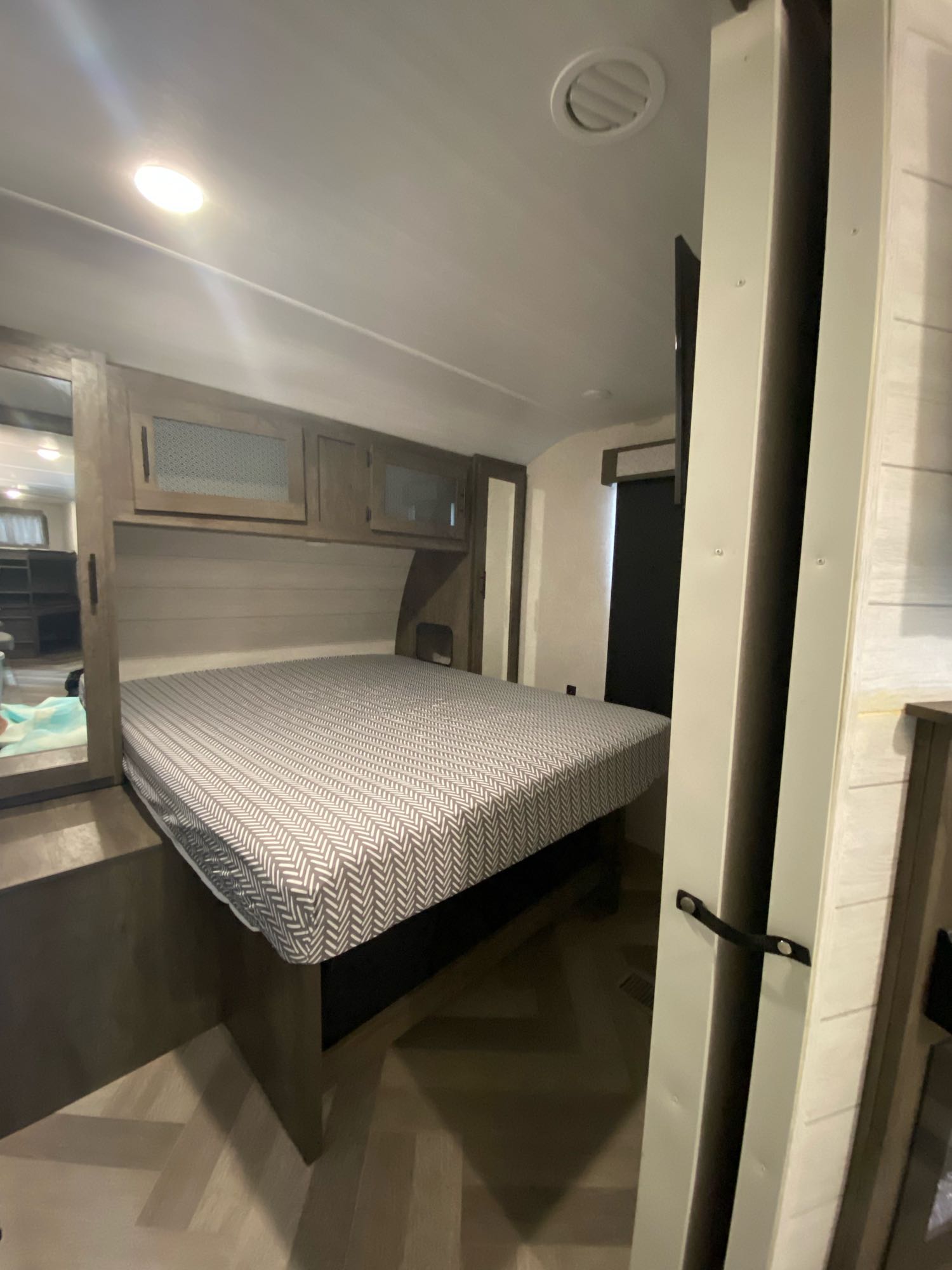Inside an RV rental, showcasing a comfortable bedroom with a patterned mattress, overhead cabinets, and clever compact design.. Forest River Wildwood 2021