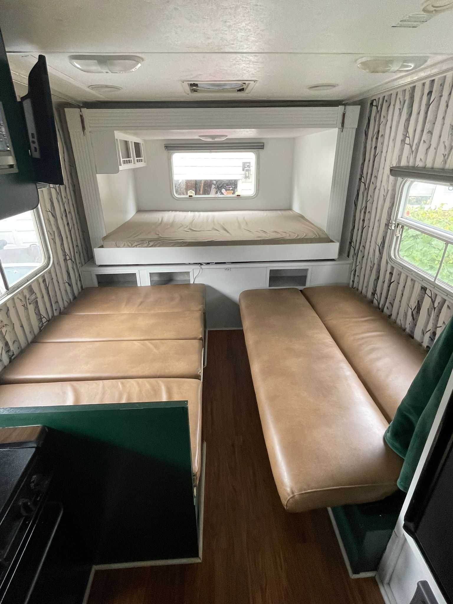 View of an RV rental's versatile interior: a raised sleeping bunk, two long tan bench seats, & kitchen space.. Forest River Surveyor 2006