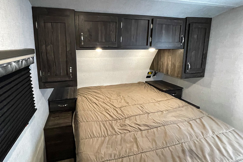 Cozy RV rental bedroom features a comfy bed with brown comforter, dark wood cabinets, and built-in nightstands.. Highland Ridge RV Open Range Ultra Lite 2020