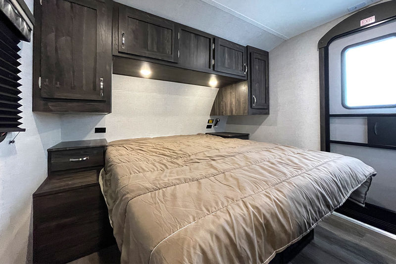 Explore this RV rental's cozy bedroom with a large bed, dark wood overhead cabinets, and a side exit door.. Highland Ridge RV Open Range Ultra Lite 2020