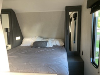 Step inside this cozy RV rental bedroom. Features a queen bed, mirrored storage cabinets, and a window for natural light.. Dutchmen Other 2022