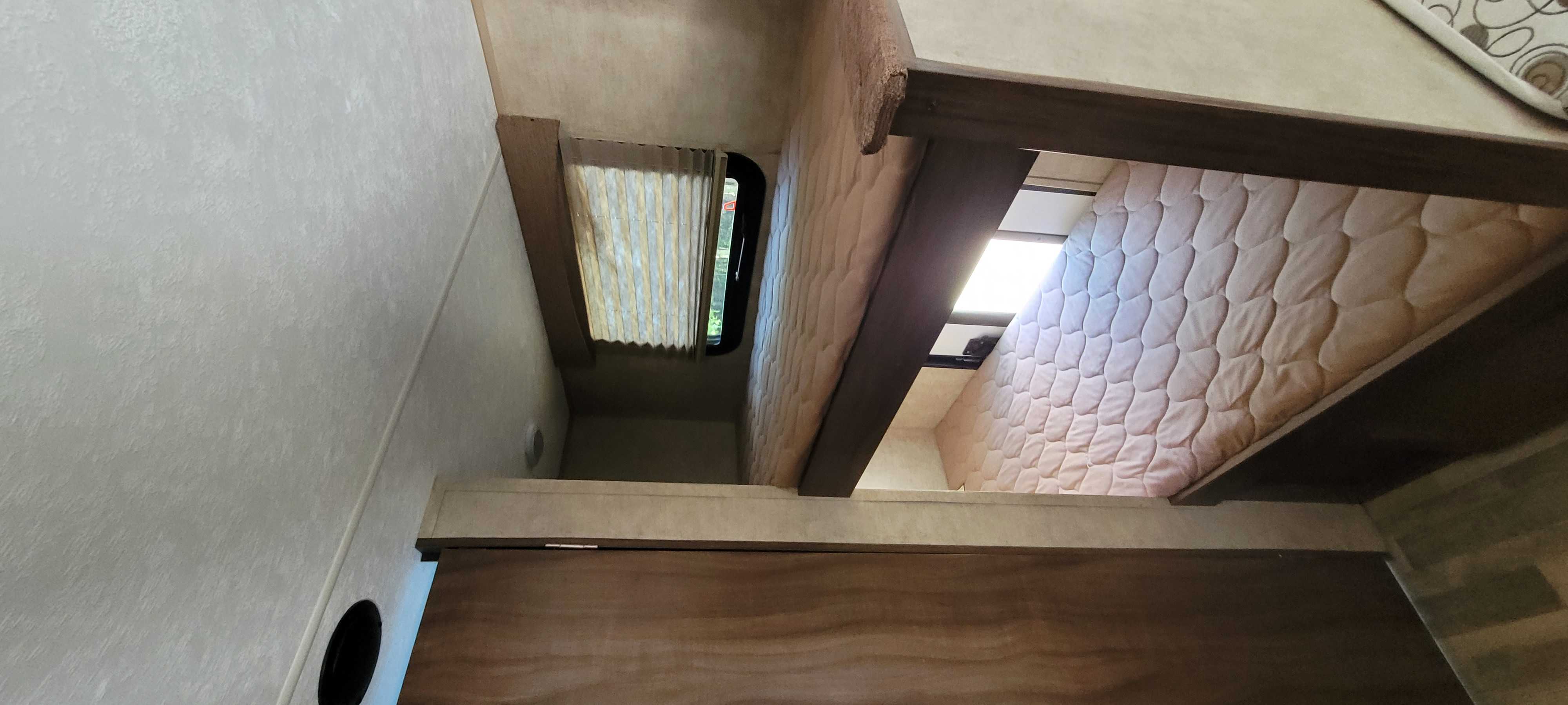 Inside an RV rental: two compact bunk beds with textured walls, window, and quilted mattresses. Perfect for travel.. Coachmen Clipper 2018