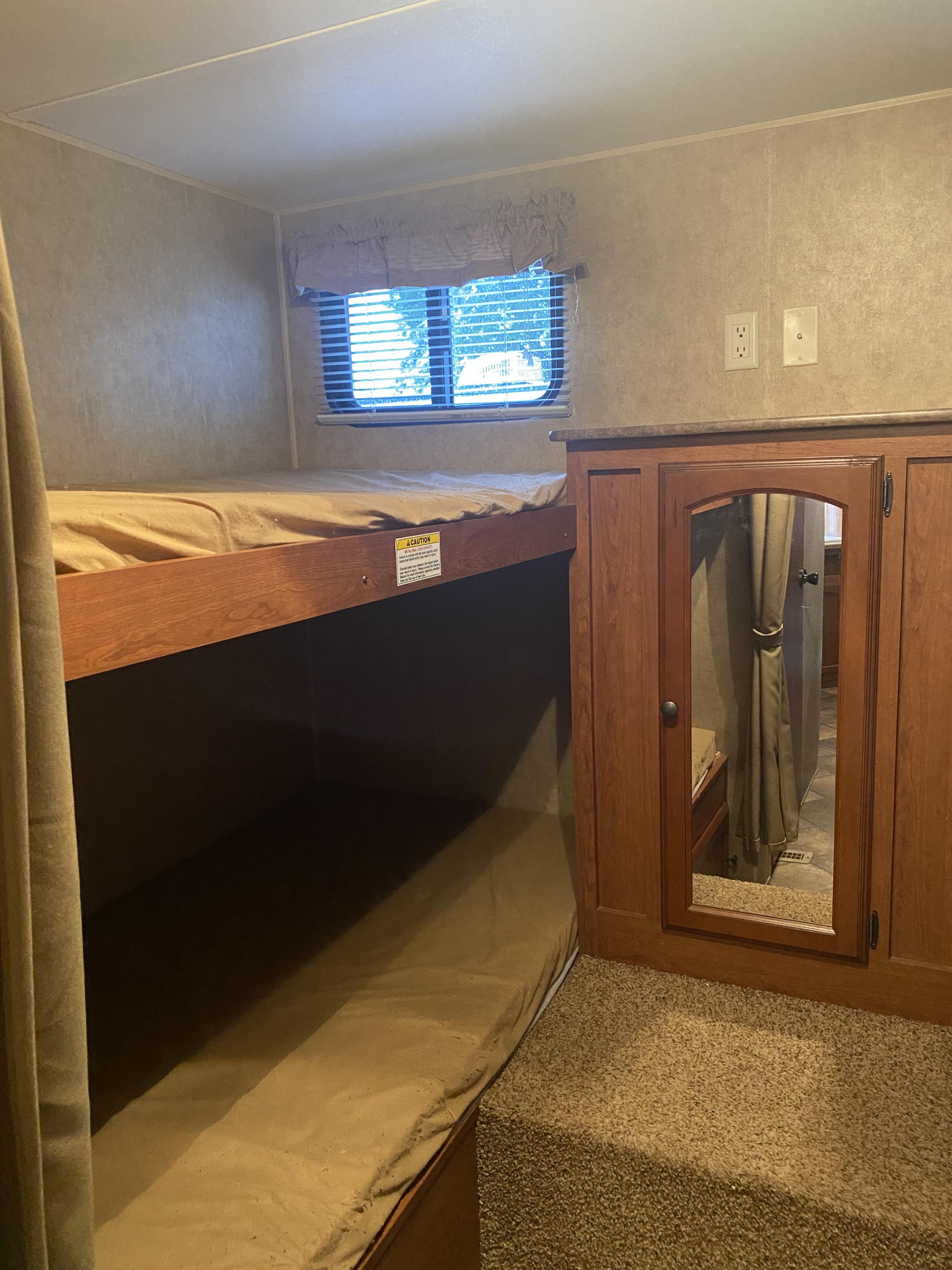 Cozy RV rental bunkhouse with top and bottom bunks, a window, and a small mirrored cabinet, ideal for family camping trips.. Dutchmen Dutchmen Trailer 2013