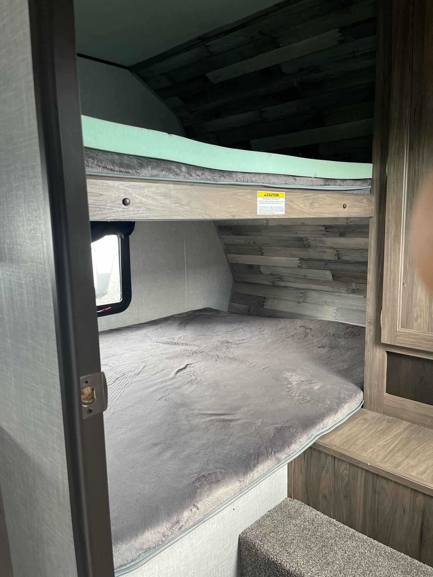 RV rental: Compact bunk beds with grey and green mattresses inside a modern RV bedroom, featuring a window and wood paneling.. Crossroads RV Zinger 2020