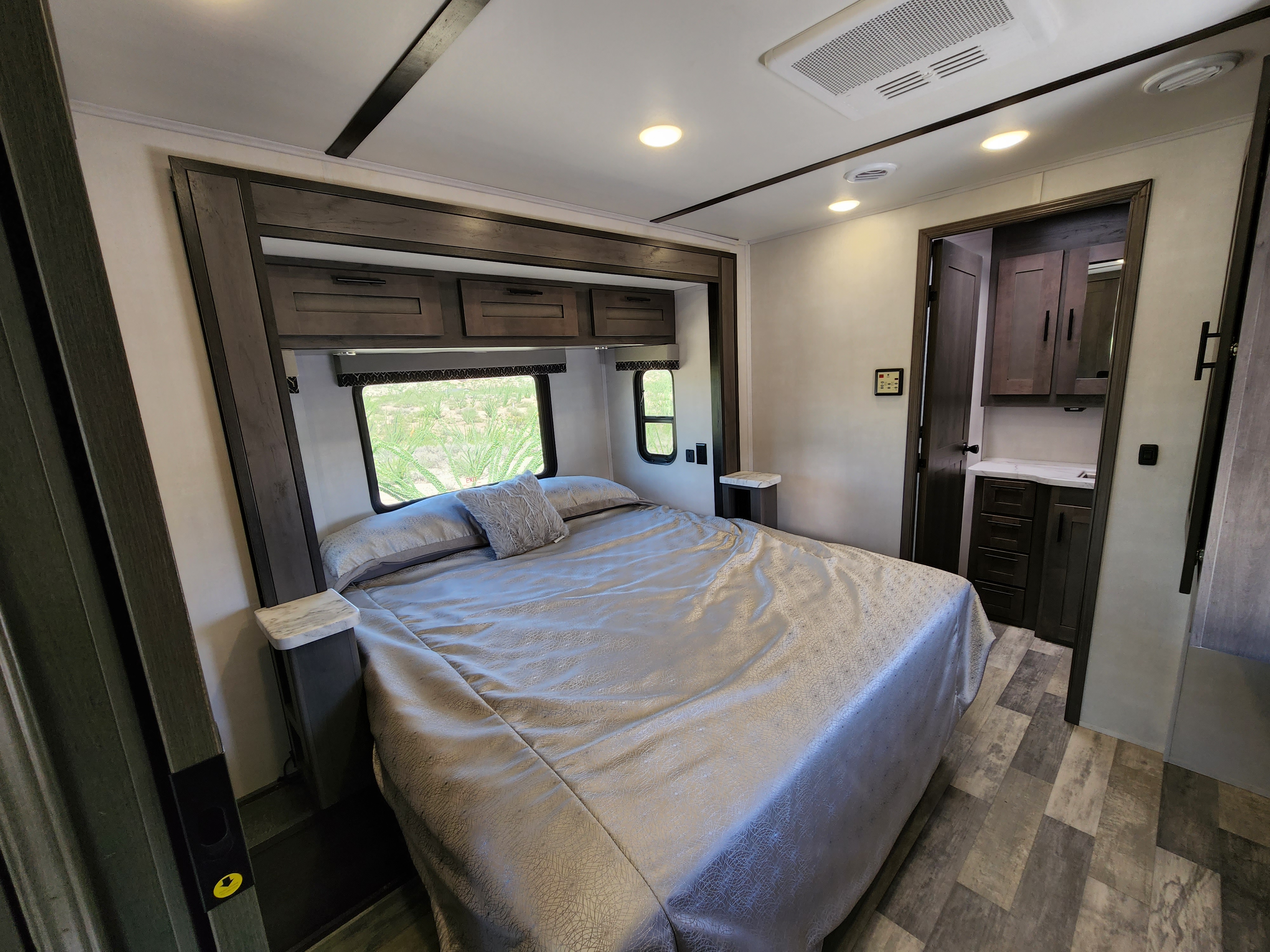 Spacious RV rental bedroom with a large bed, dark wood overhead cabinets, and adjacent compact vanity/bathroom area.. Forest River FR3 34DS 2022