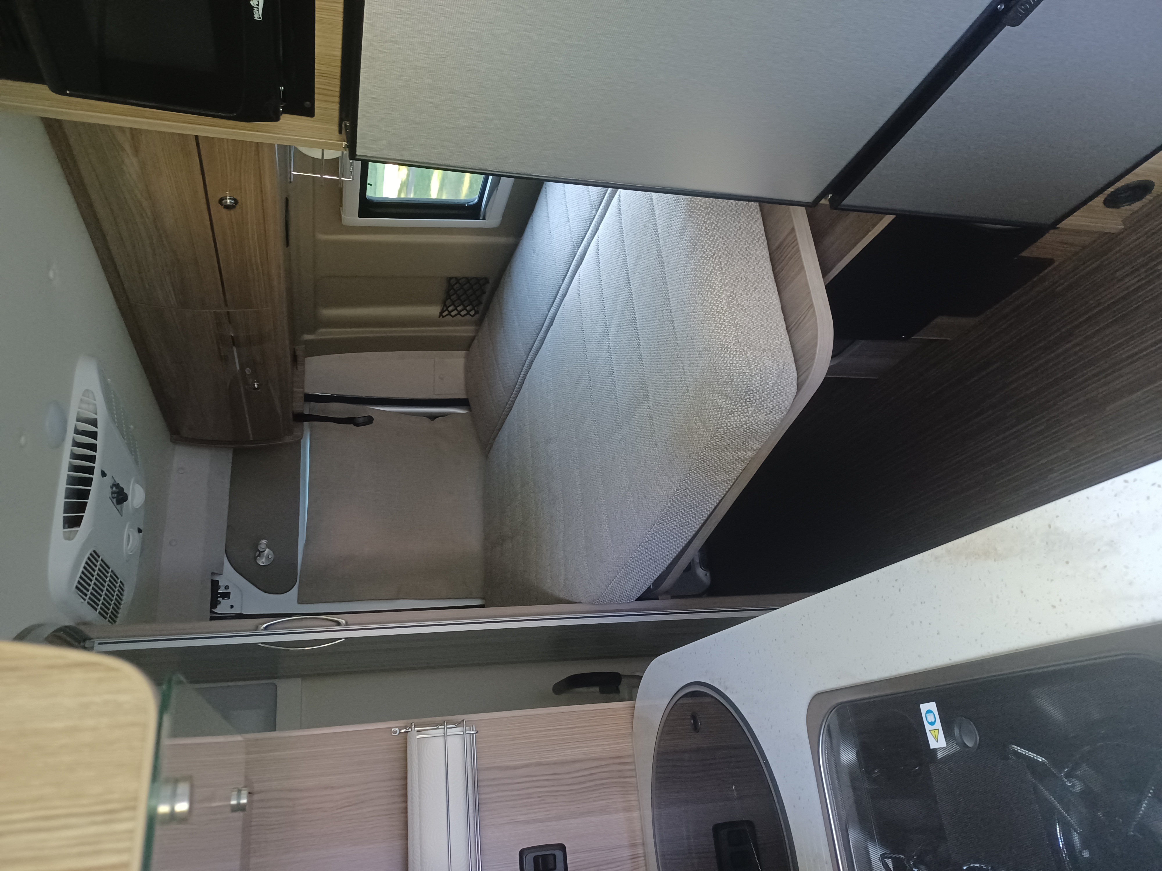 Inside an RV rental: a compact living space with a comfy bed, kitchen counter, sink, storage, and an AC unit.. Winnebago Travato 2020