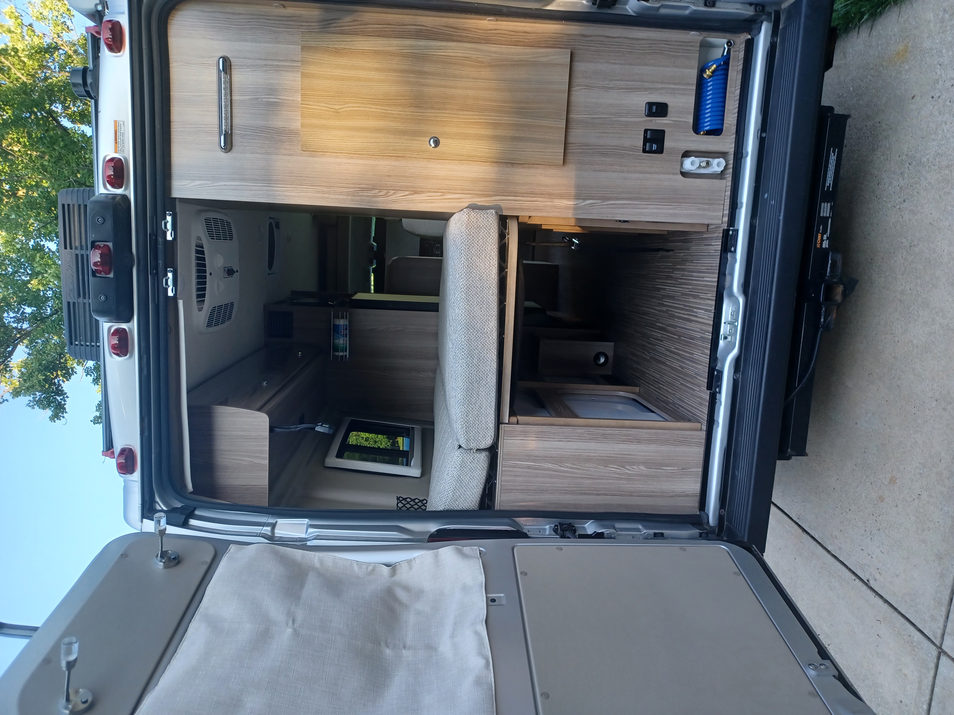 Inside an RV rental looking forward from open rear doors, featuring a multi-functional bed, wood cabinetry, and ample storage.. Winnebago Travato 2020
