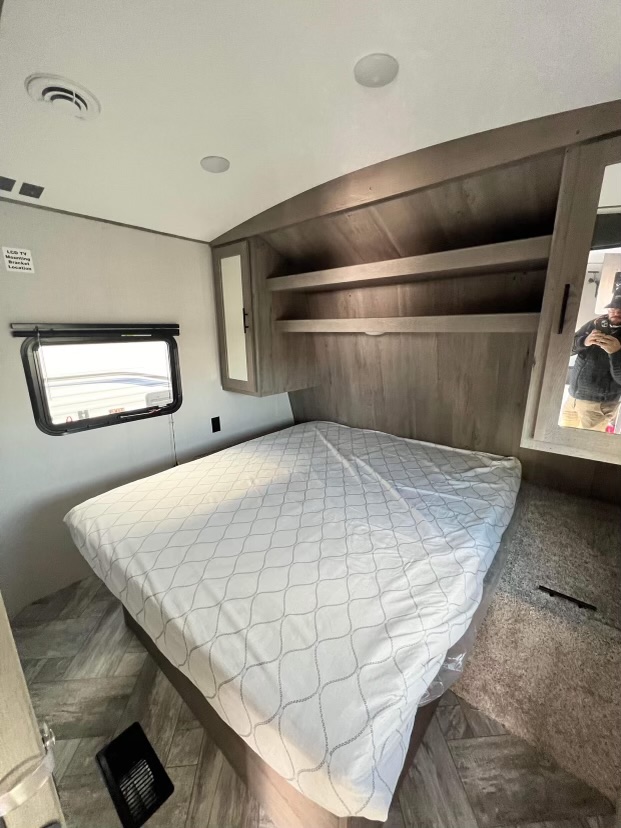 Experience comfort in this RV rental bedroom. Features include a large bed, overhead storage, window, and TV mount.. Keystone RV Springdale 2021