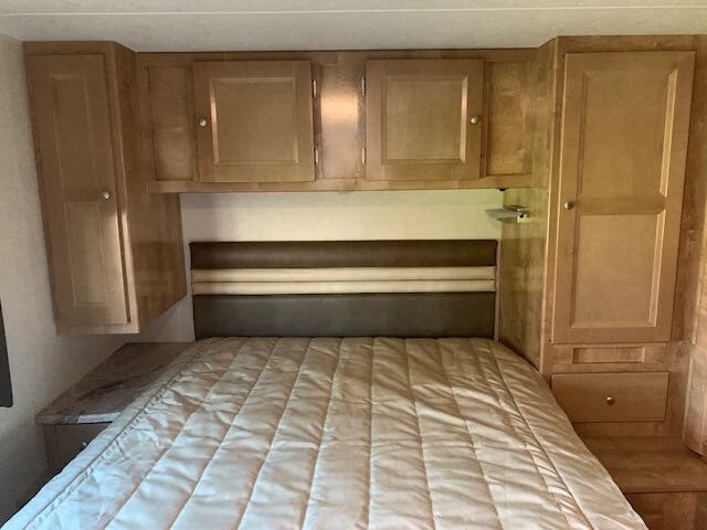 Cozy RV rental bedroom with ample cabinet storage above and beside the bed, plus an upholstered headboard.. Forest River Coachmen Leprechaun 2019