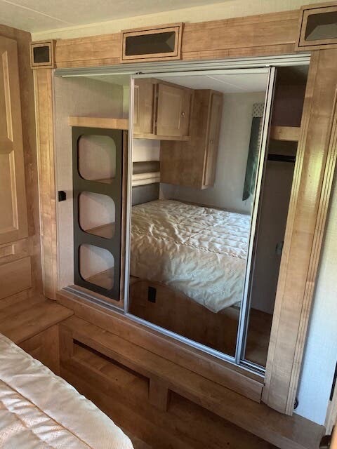 RV rental bedroom with mirrored closet doors, built-in storage, and warm wood finishes, offering comfort and space.. Forest River Coachmen Leprechaun 2019