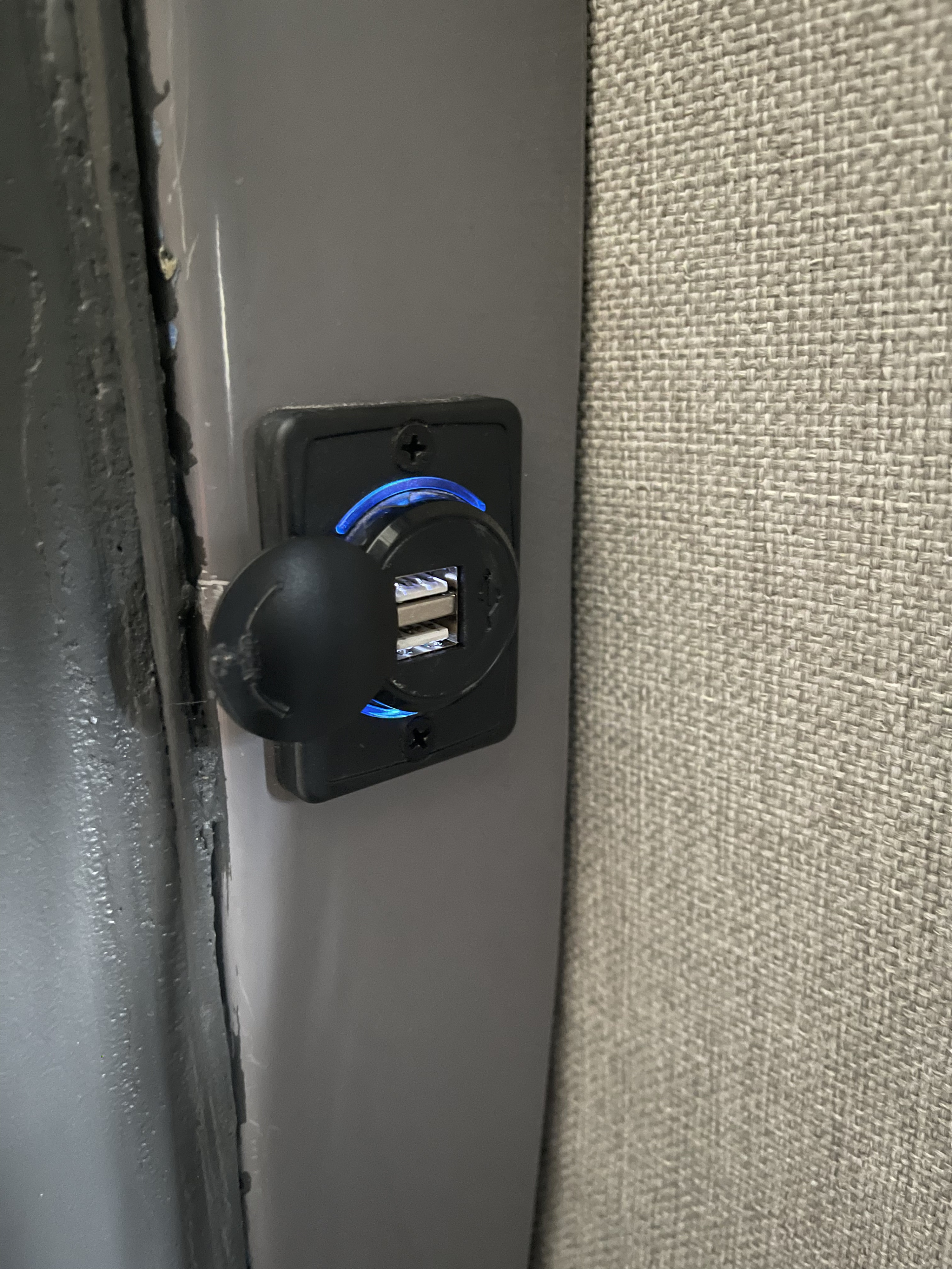 This RV rental features a dual USB charging port with a blue LED, mounted on a gray panel next to a textured wall.. Mercedes Sprinter 2019