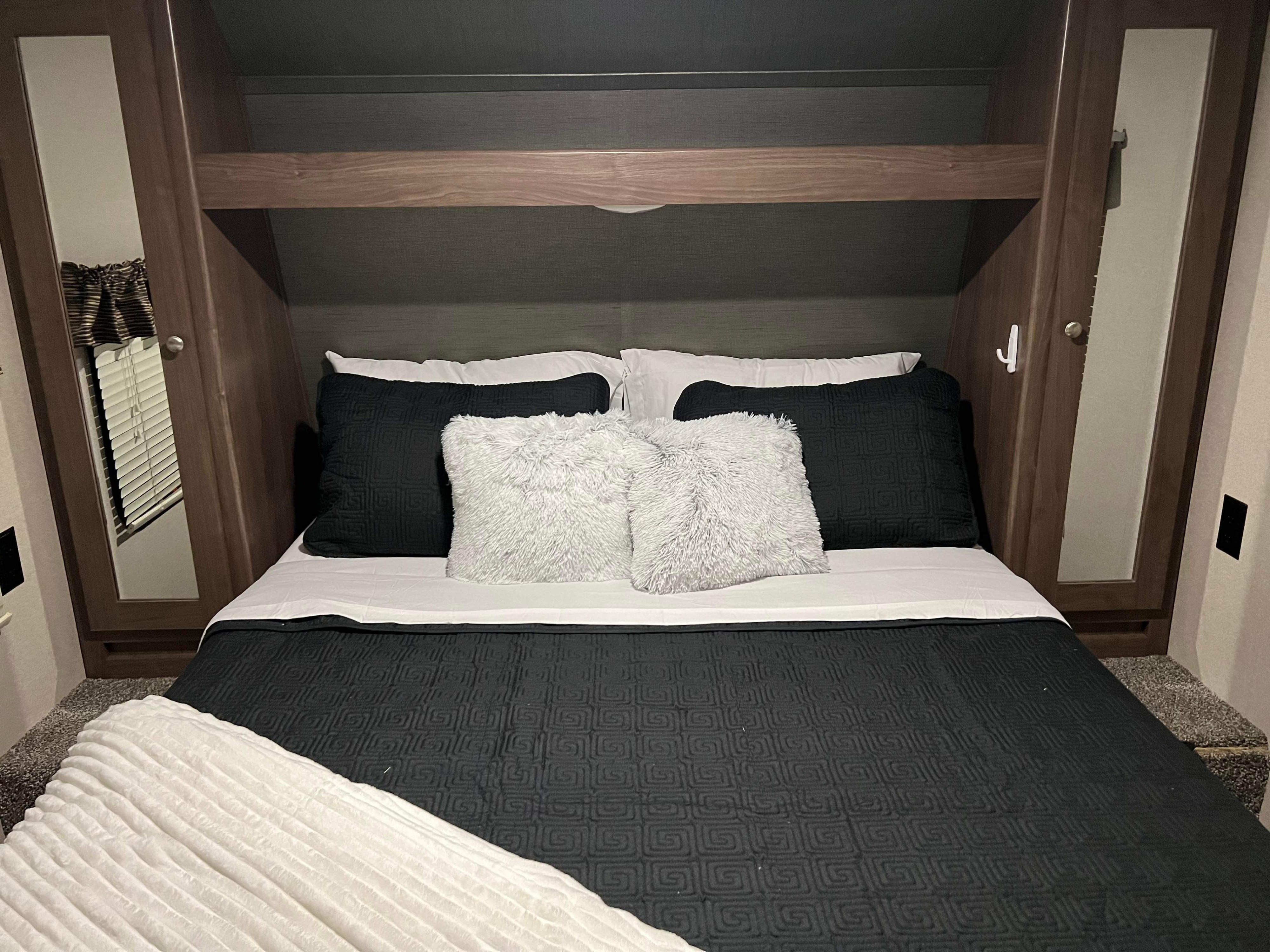 Inside a clean RV rental bedroom: a bed with black/white bedding, fluffy pillows, overhead storage, and mirrored closets.. Keystone RV Hideout 2018
