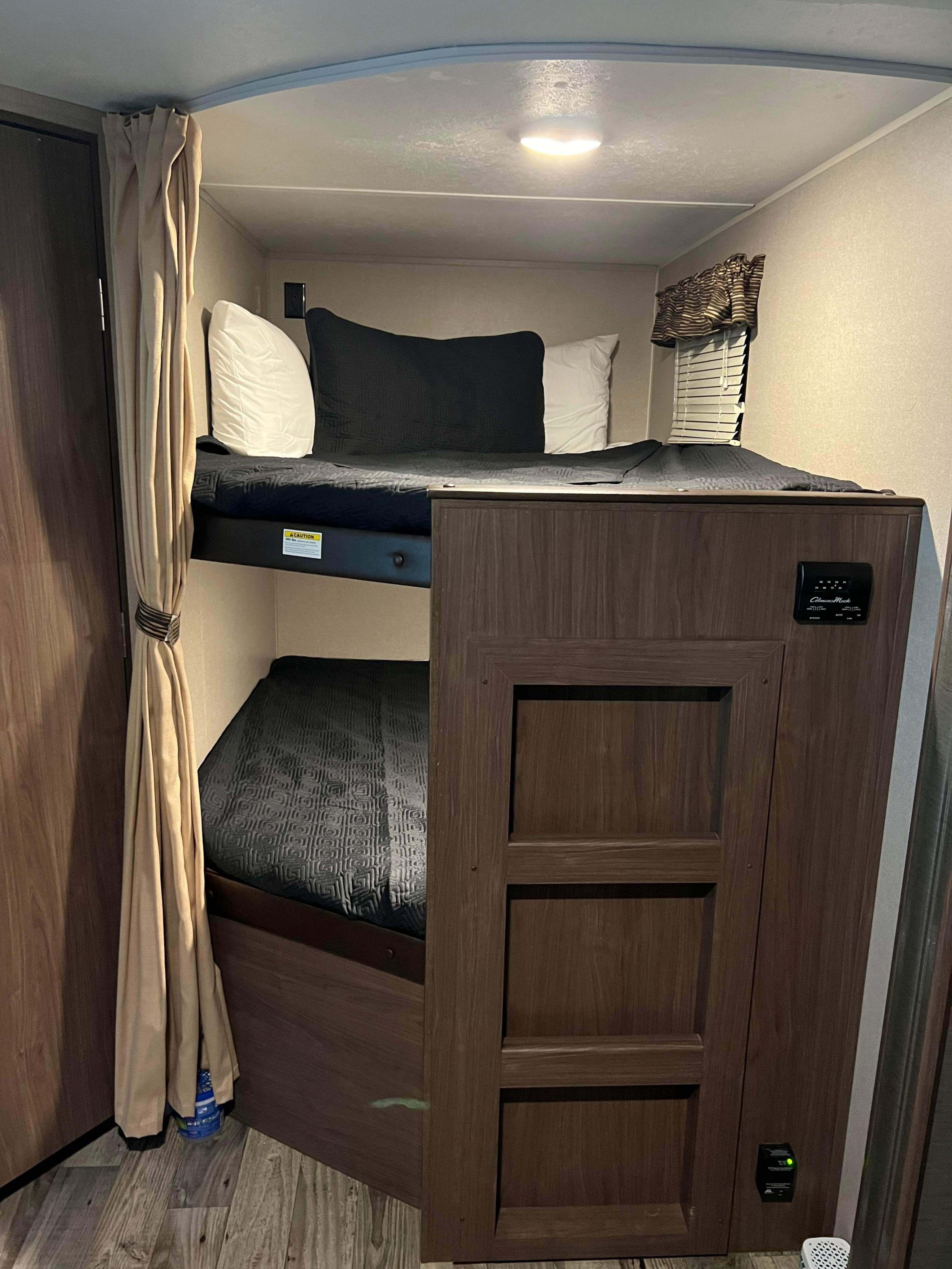 Cozy bunk beds in an RV rental, featuring a privacy curtain, individual lighting, and climate control panel.. Keystone RV Hideout 2018