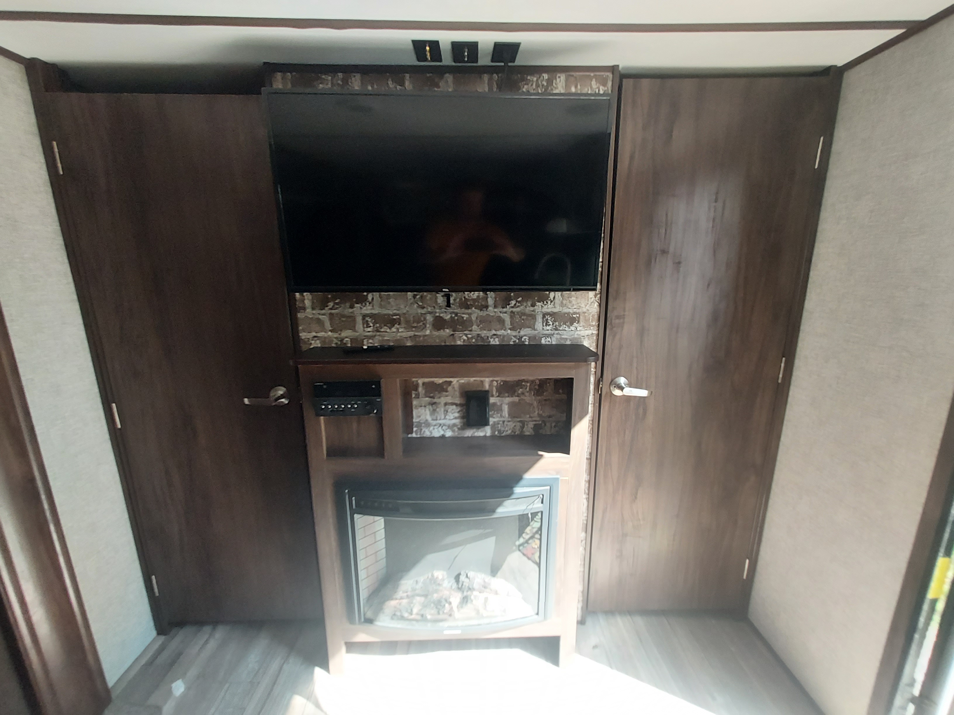 Cozy RV rental interior: an entertainment console with TV & electric fireplace, flanked by dark wood storage cabinets.. Forest River Cherokee Alpha Wolf 2019