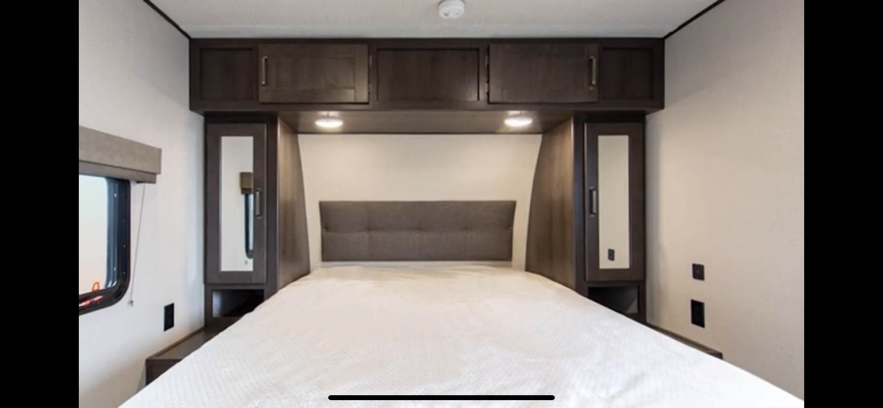 RV rental bedroom with a comfortable bed, dark wood overhead cabinets, and mirrored wardrobes.. Grand Design Transcend Xplor 2021