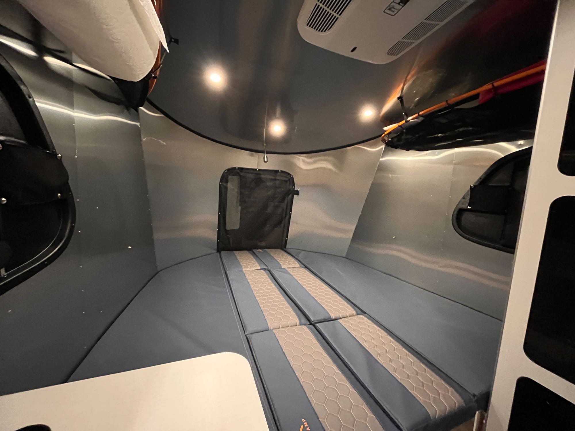 Cozy aluminum interior of an RV rental, showing a modular sleeping area with cushioned mats and overhead lighting for comfortable travel.. Airstream Basecamp 2022