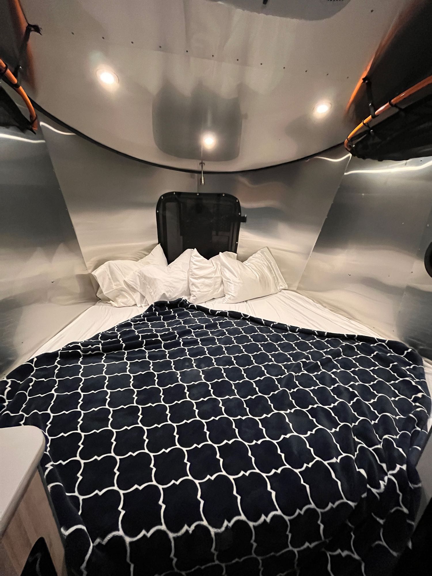 Cozy RV rental: Modern bed with white linens & a dark, patterned blanket inside a sleek metallic interior.. Airstream Basecamp 2022