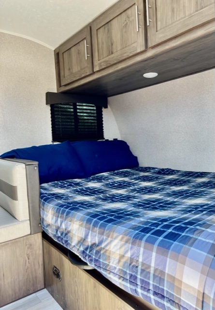 RV rental sleeping space: A bed with blue plaid comforter, pillow, overhead cabinets, and window, for comfort on the road.. Clipper Clipper Trailer 2021