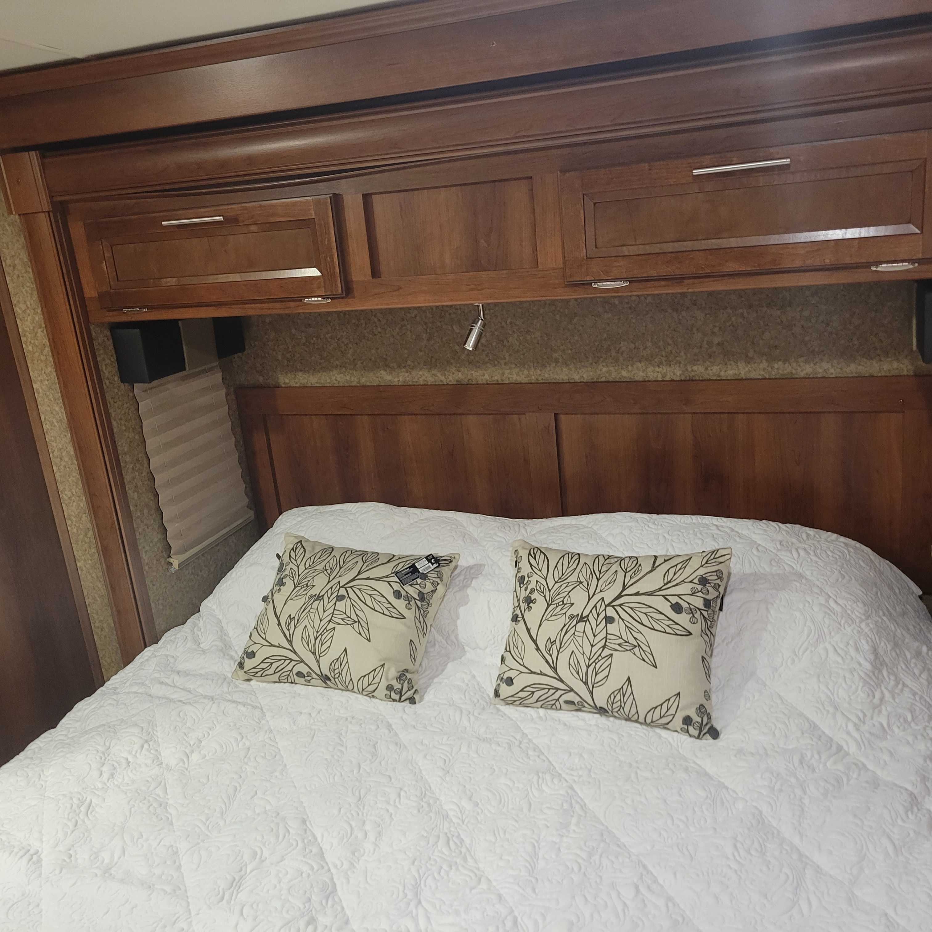 Relax in this cozy RV rental bedroom. Features a large bed with white quilted bedding, patterned pillows & wood overhead storage.. Forest River Fr3 2015