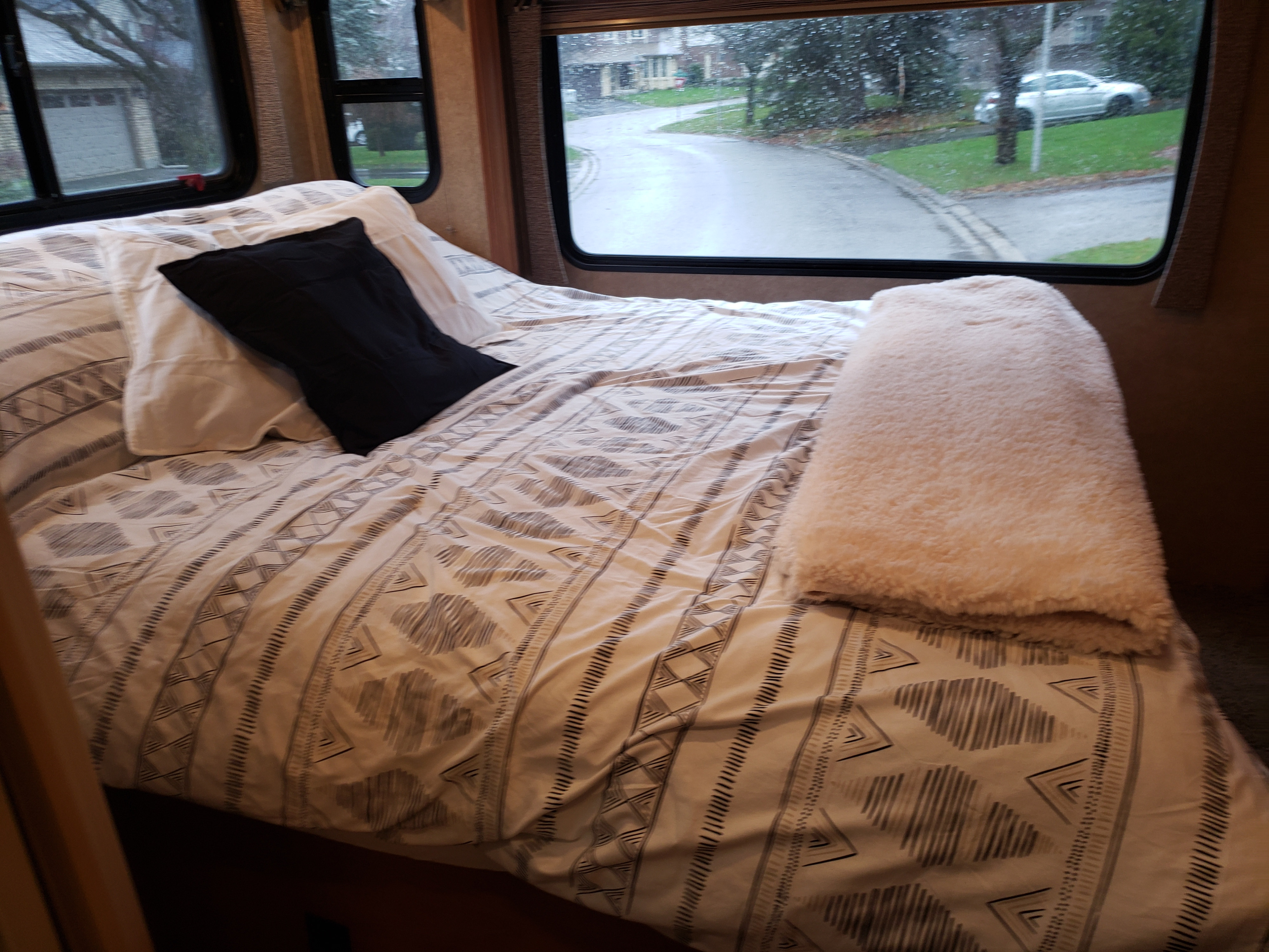 Cozy RV rental bedroom with patterned bedding and a view of a rainy street from the window.. Forest River Sunseeker 2015