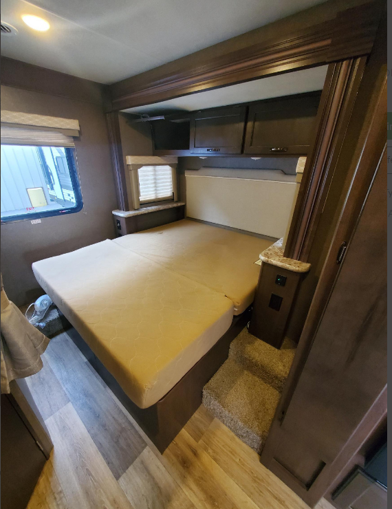 Discover this cozy RV rental bedroom. Features a large bed, overhead cabinets, and steps, offering comfort for your travels.. Thor Freedom Elite 2019