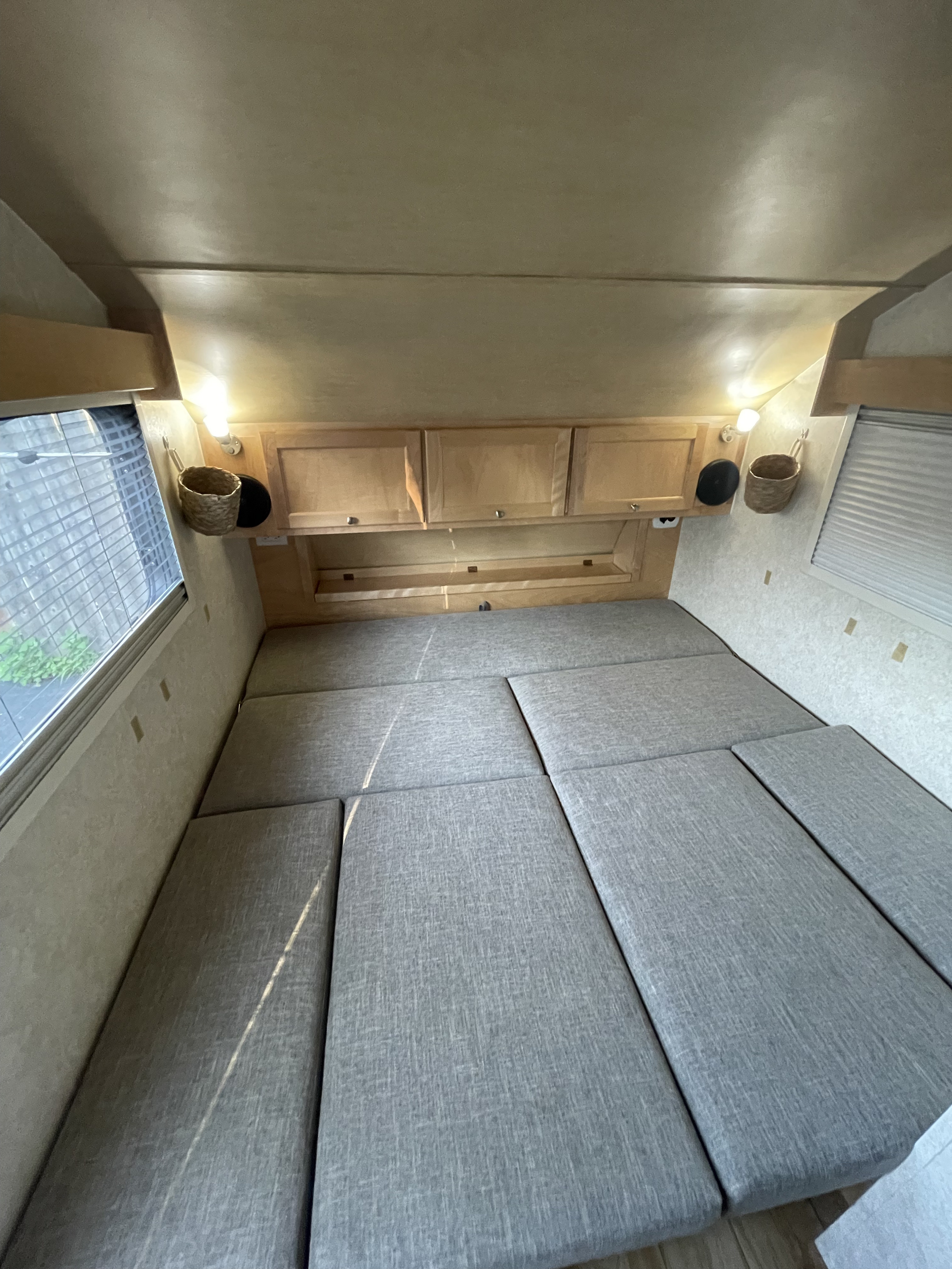 RV rental interior showcasing a spacious gray bed, overhead storage, and wall-mounted lights.. nuCamp T@B 2018