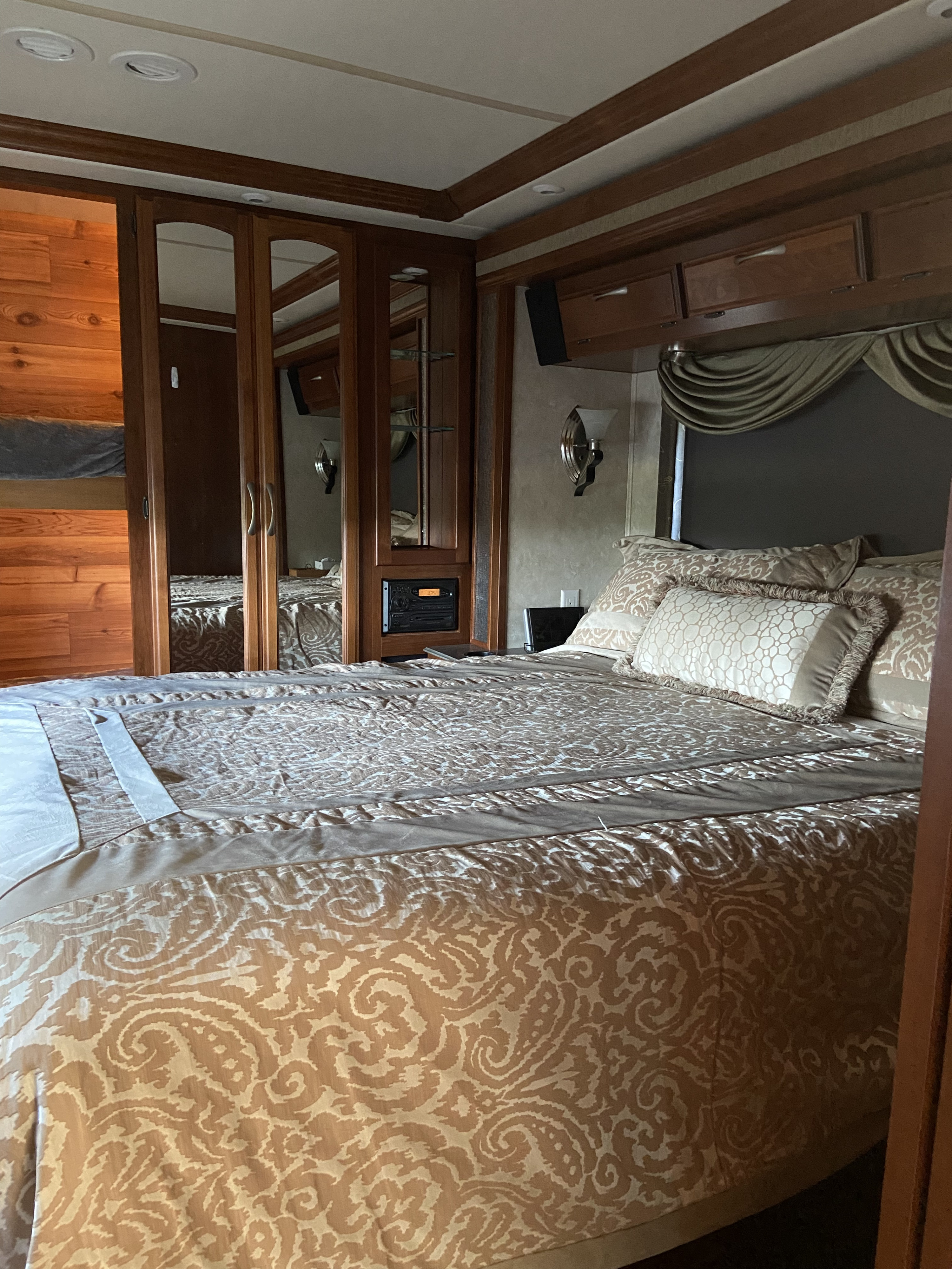 Inviting RV rental bedroom with patterned bedding, mirrored storage, and elegant wood interior for a comfortable stay.. Fleetwood Providence 2005