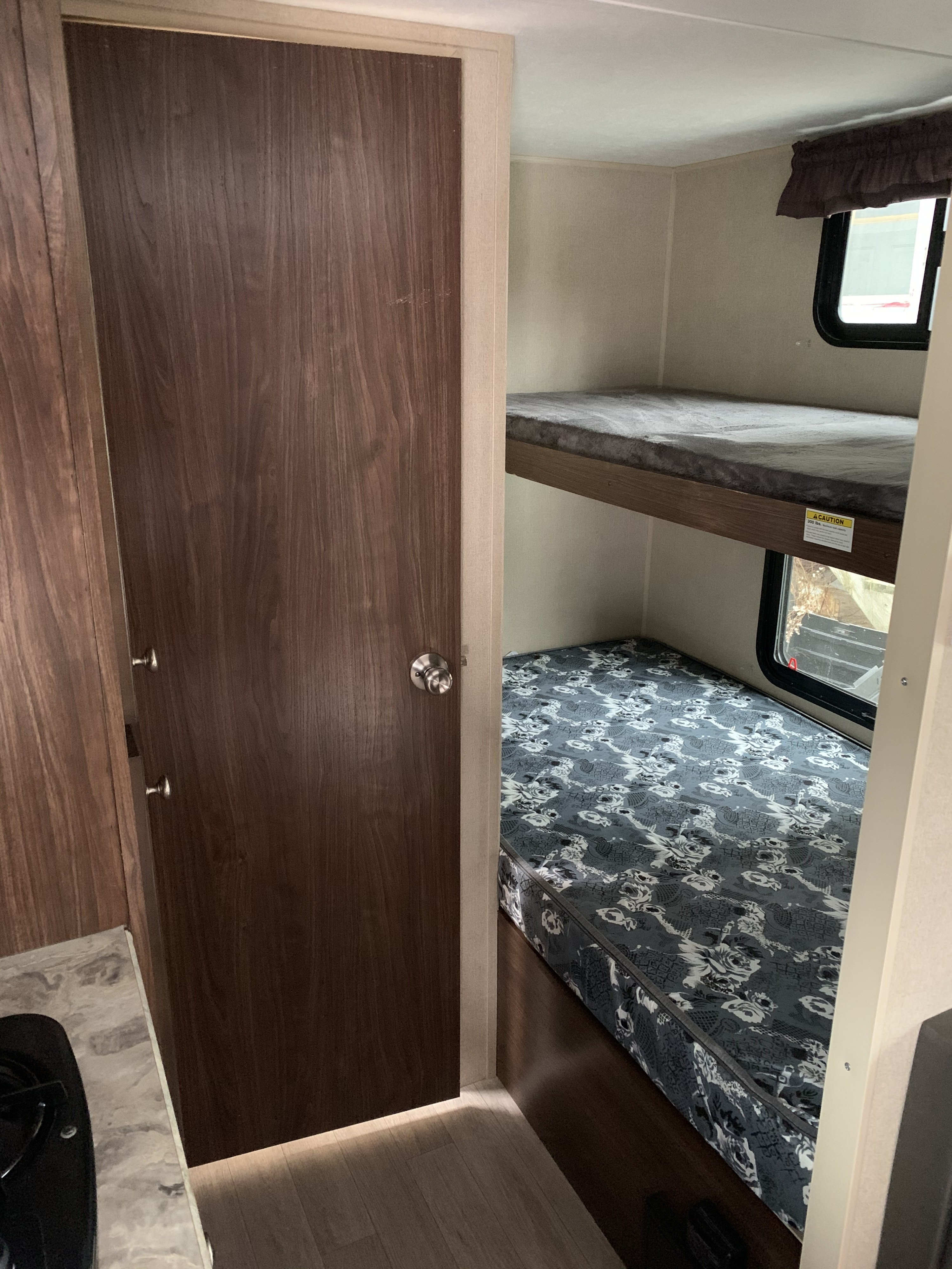 RV rental interior with a dark wood door leading to cozy bunk beds, offering compact sleeping in a travel trailer.. Coleman 17F 2017