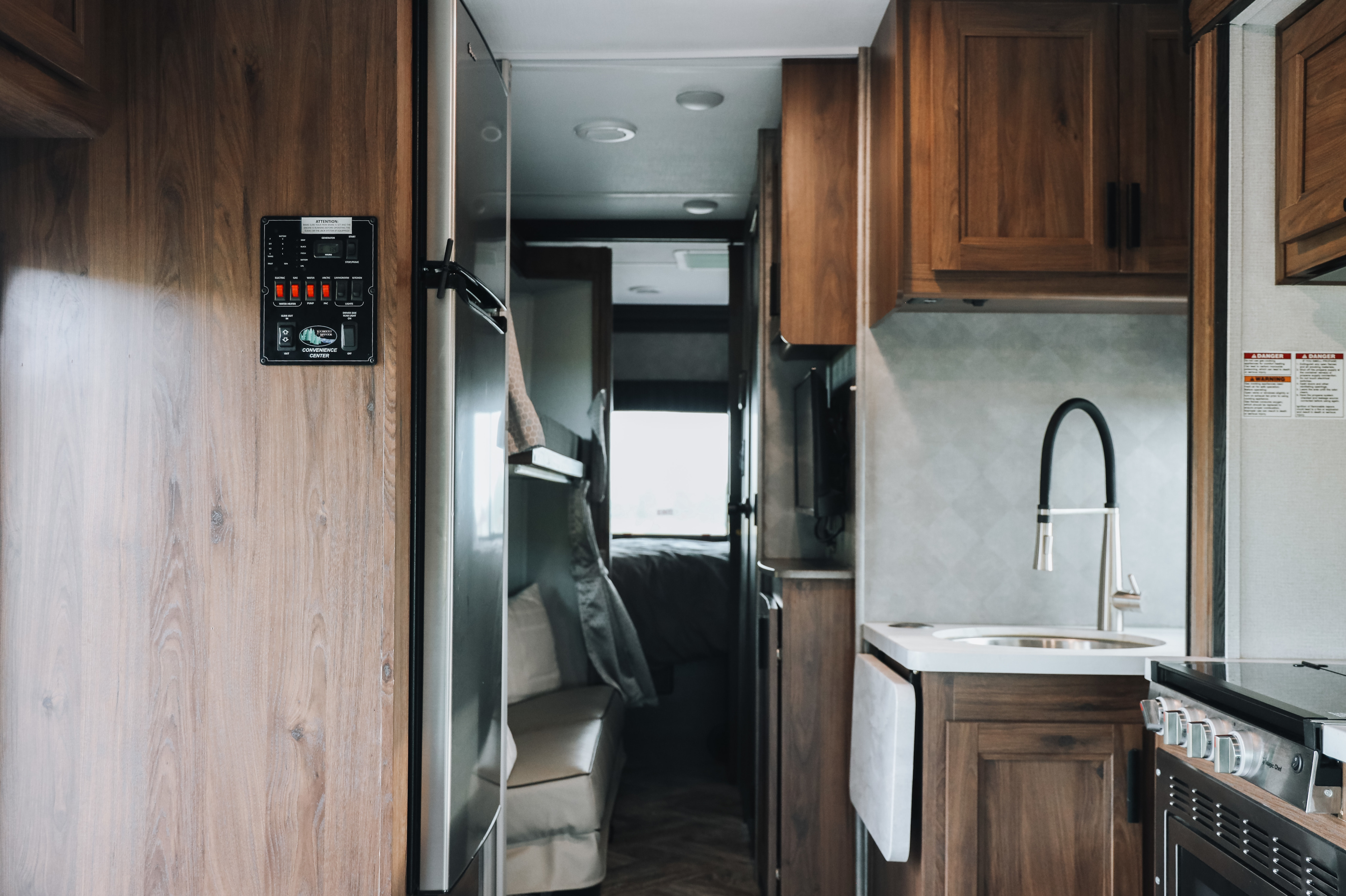 Interior of an RV rental showing a kitchen with sink, stove, wood cabinets, and a control panel on the left wall.. Forester LE 2021