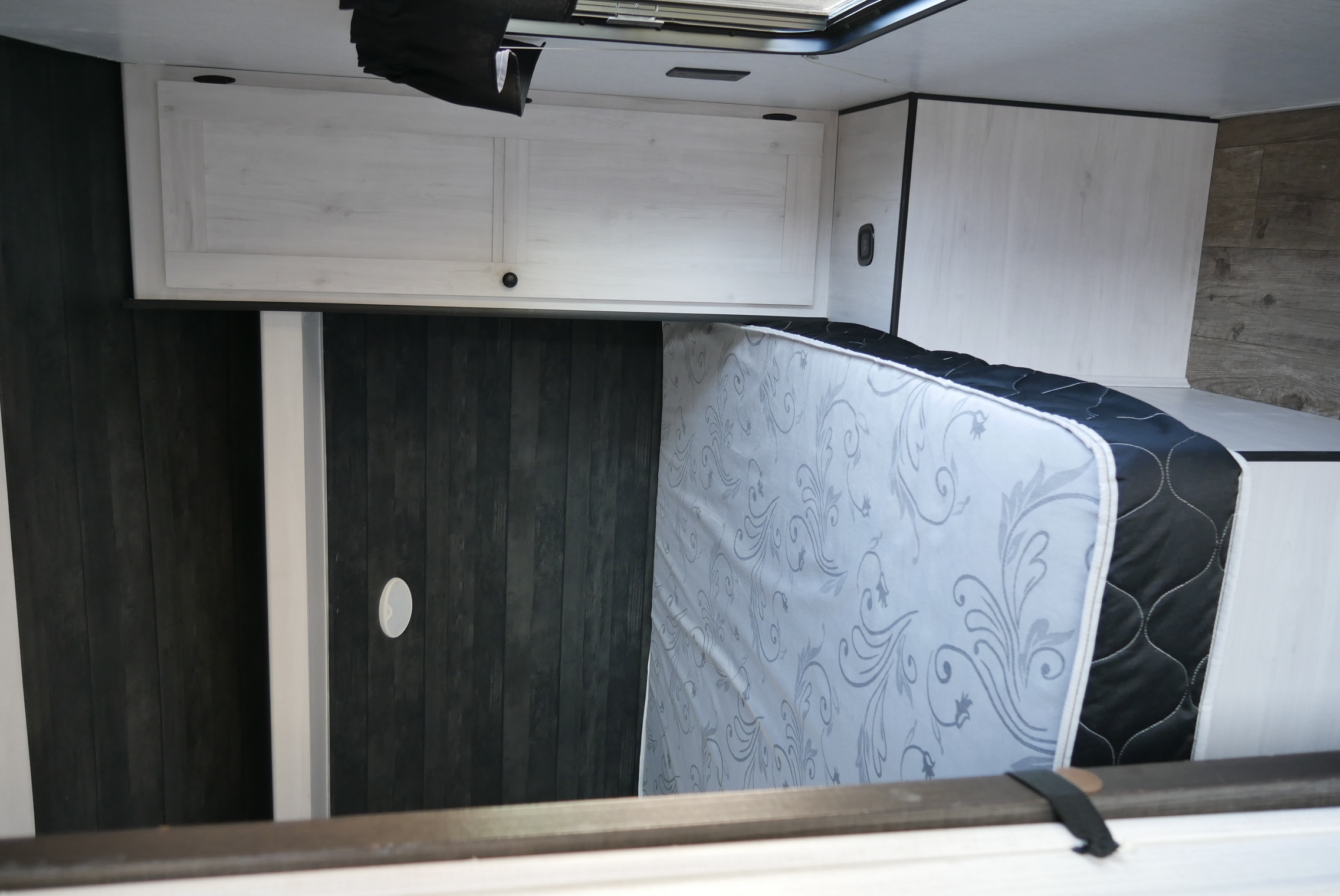 RV rental interior: A compact sleeping area with a partially lifted mattress, white overhead cabinets, and dark paneled walls.. Heartland RVs Trailrunner 2021