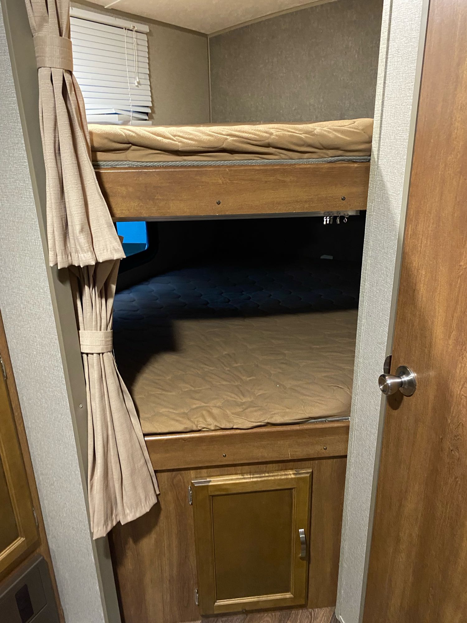 Interior of an **rv rental**: two stacked bunk beds with mattresses, tied-back curtains, and a lower storage cabinet.. keystone Springdale 2017
