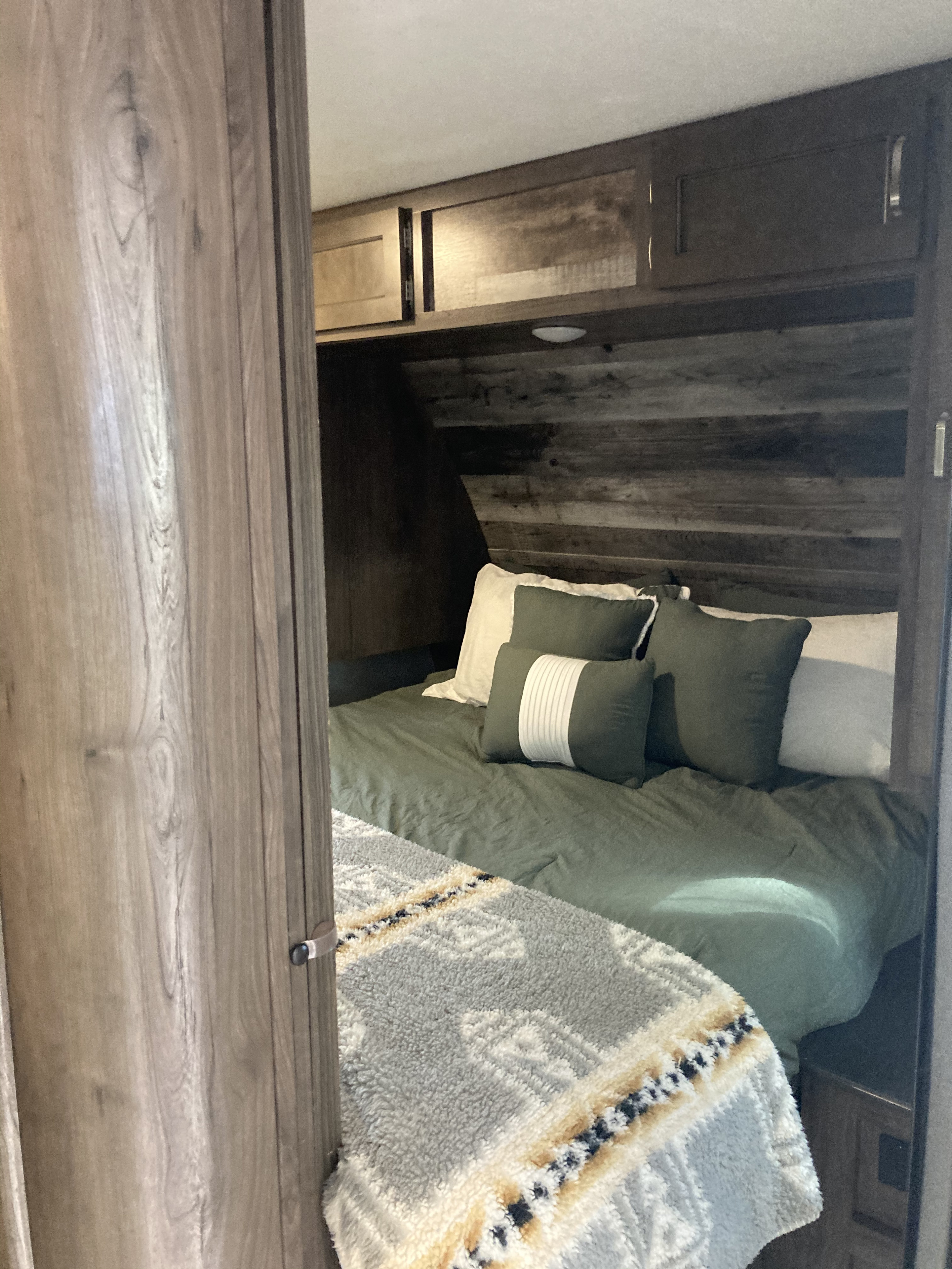Cozy RV rental bedroom featuring green bedding, a patterned blanket, wood paneling, and overhead storage.. Keystone RV Passport SL 2020
