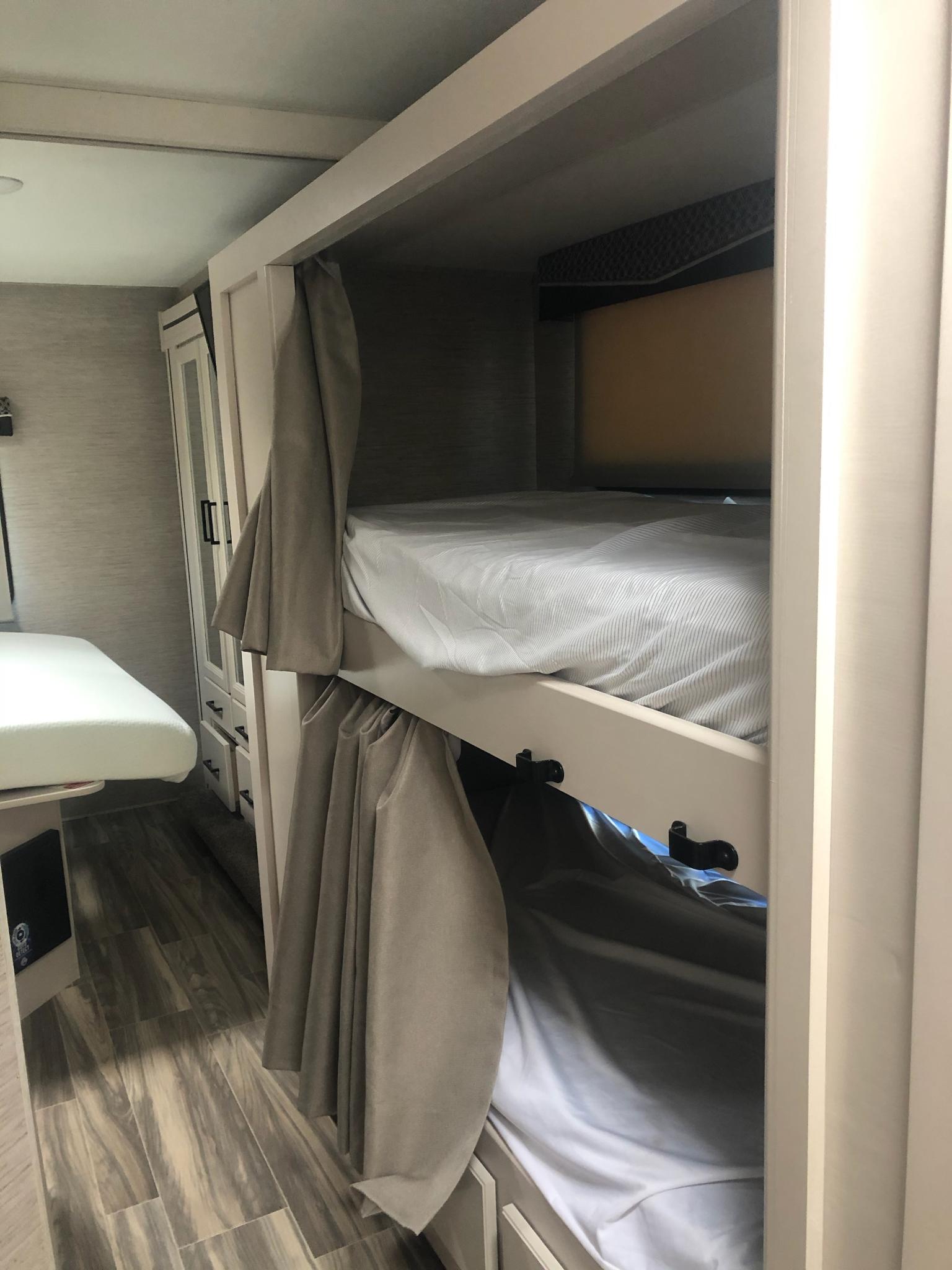 RV rental interior features compact bunk beds with privacy curtains, wood-look flooring, and white cabinetry.. Thor Motor Coach Chateau 2023