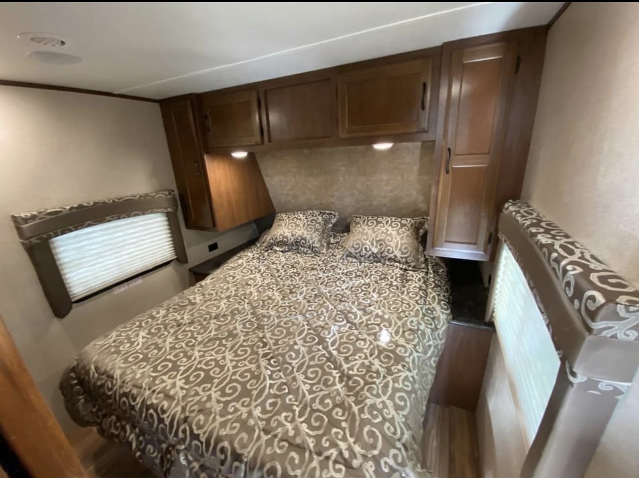 Cozy RV rental bedroom featuring a comfy bed with patterned bedding, overhead cabinets, and a window for a functional space.. Jayco Jay Flight 2016