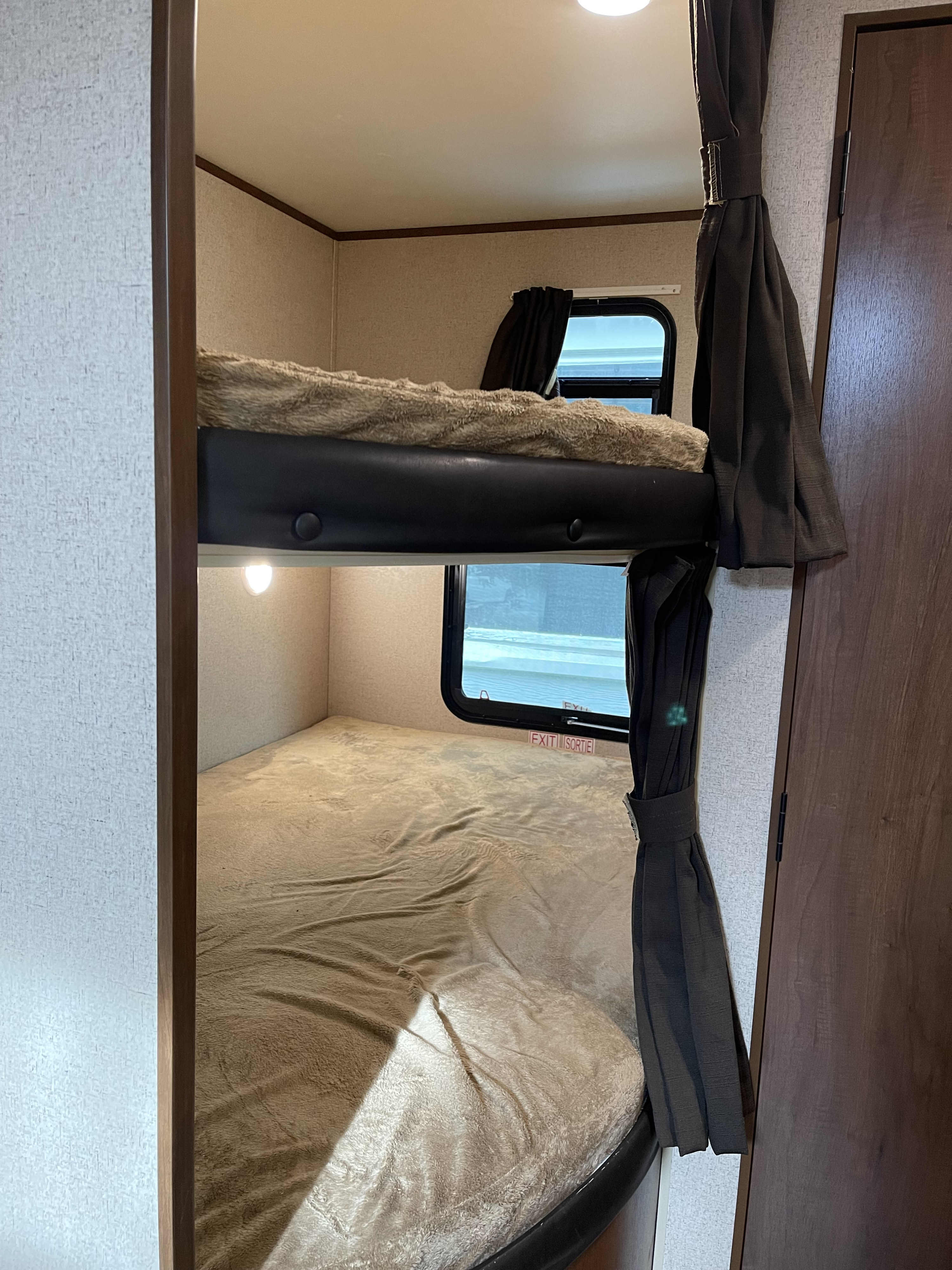 RV rental's cozy sleeping area with upper and lower bunk beds, windows, and tied-back curtains.. Jayco Jay Flight 2016