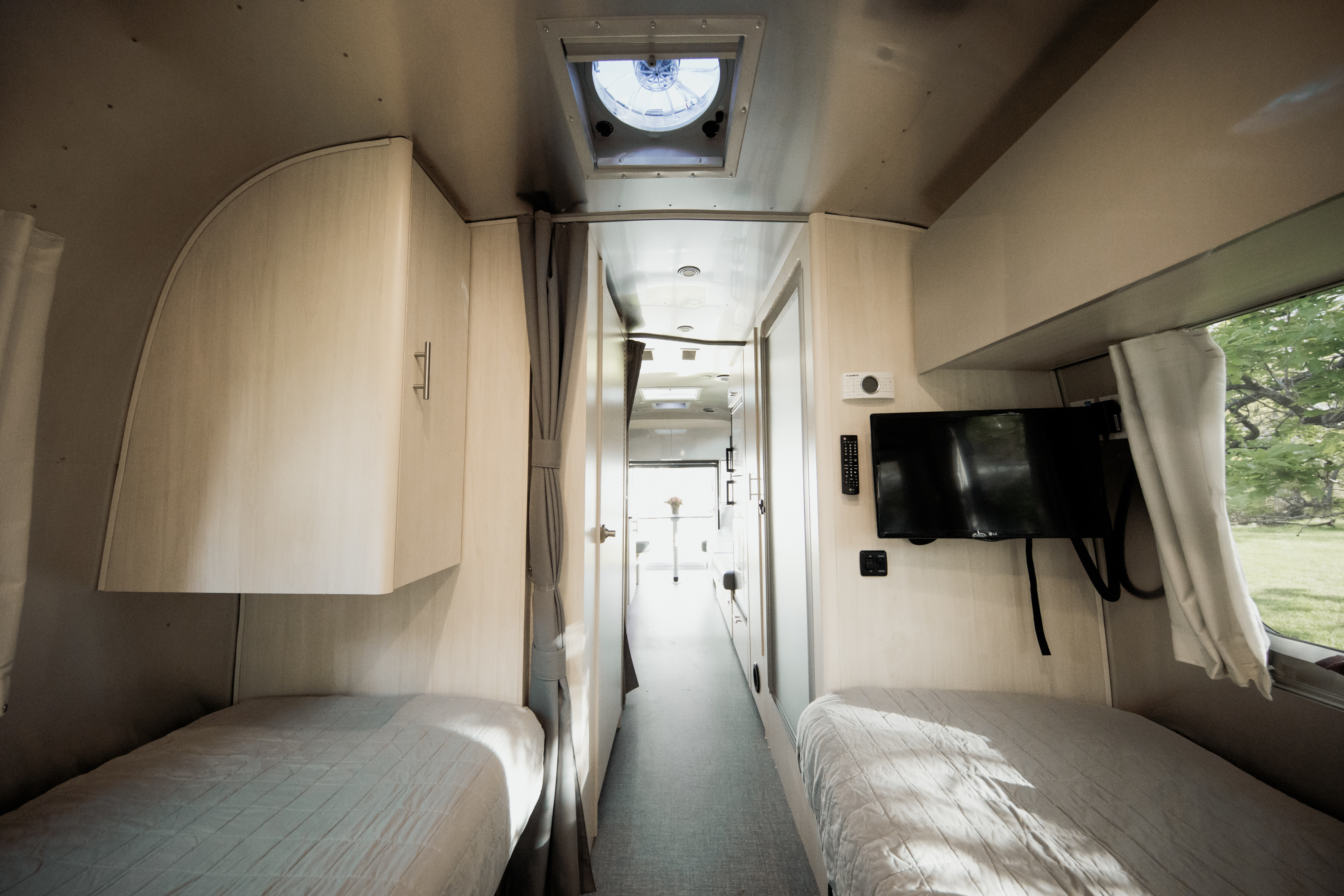 Inside a comfortable RV rental: Twin beds, overhead cabinets, TV, and a view of nature from this inviting camper interior.. Airstream Flying Cloud 2021
