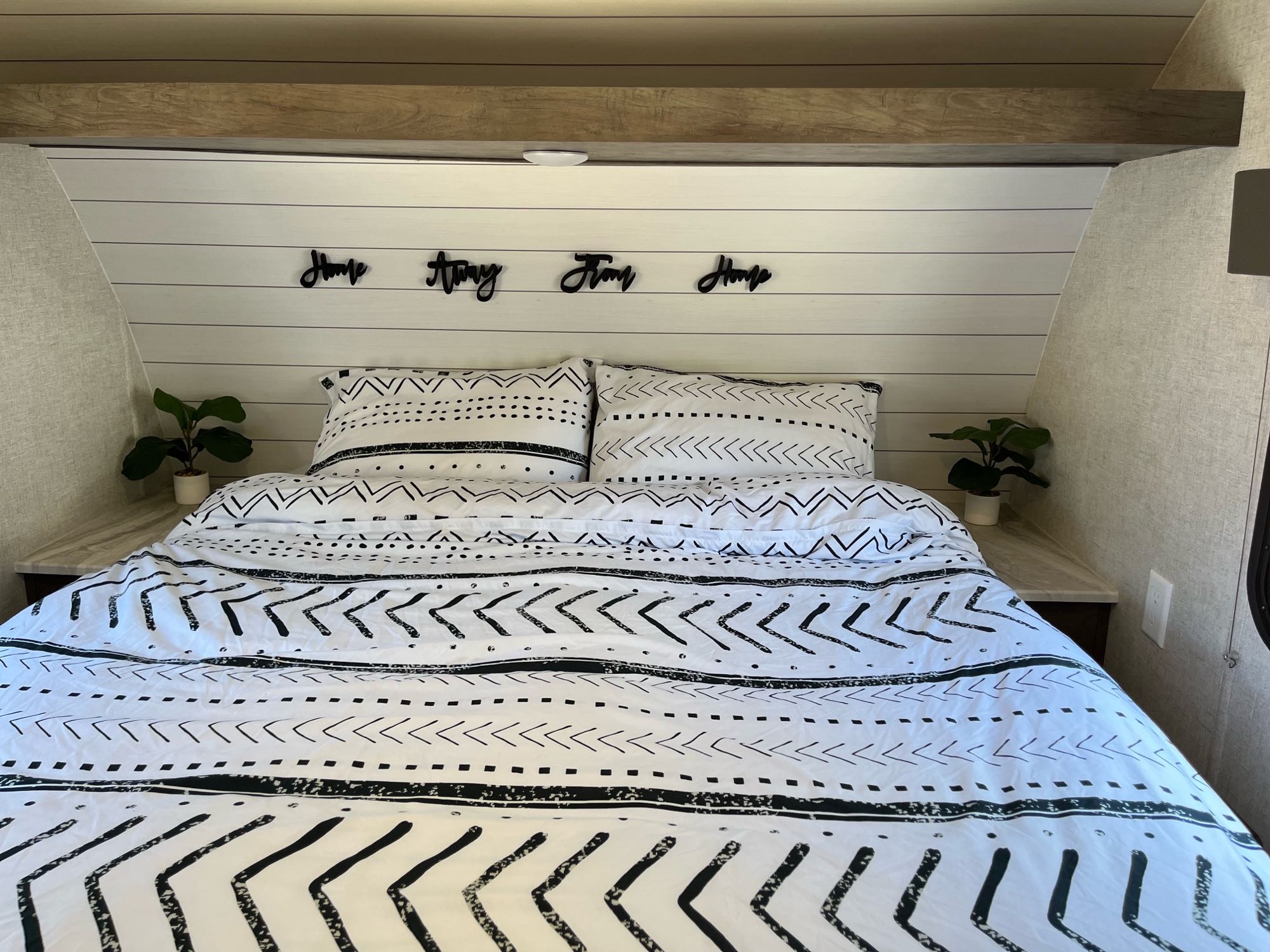 Cozy RV rental bedroom featuring a black and white patterned bed, shiplap headboard, and "Home Away From Home" decor.. Forest River Wildwood X-Lite 2021
