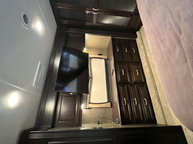Inside an RV rental: Bedroom features a mounted TV, dark wood cabinets, and a bed. Provides ample storage.. Berkshire XLT 2017