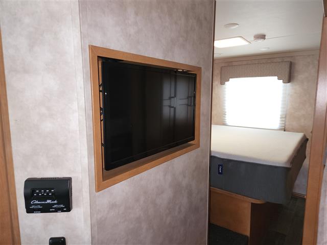This RV rental interior features a cozy bedroom with a bed, bright window, and a wall-mounted TV with a control panel nearby.. Winnebago Minnie Winnie 2018