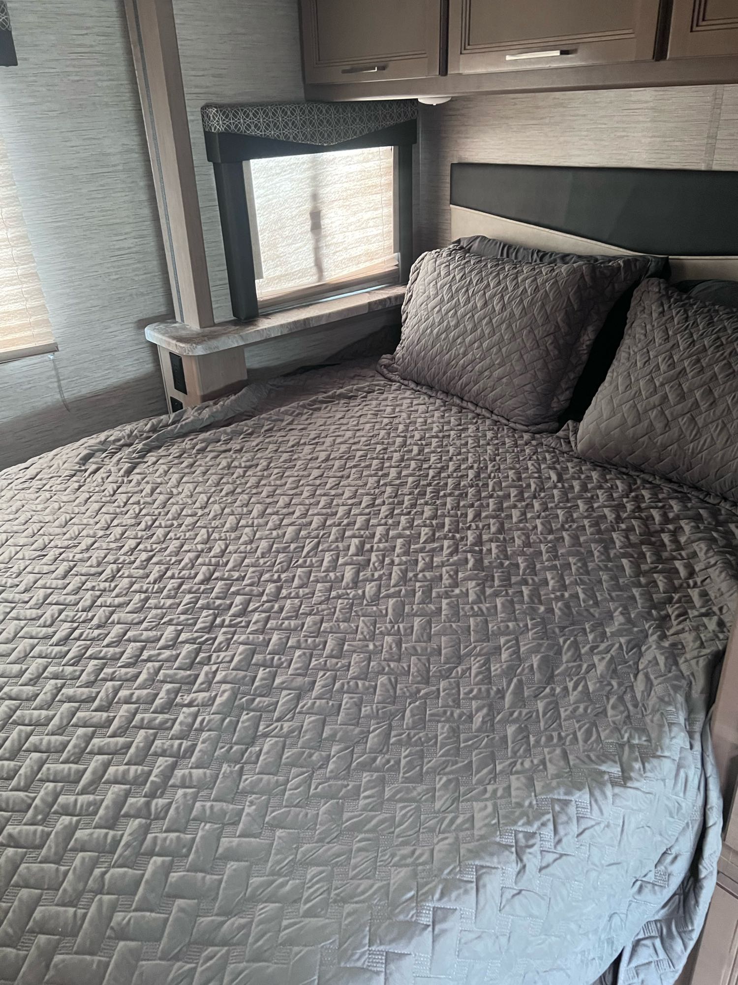 RV rental interior showing a comfortable bedroom with a grey quilted bedspread, headboard, and window.. Thor Motor Coach Four Winds 2021