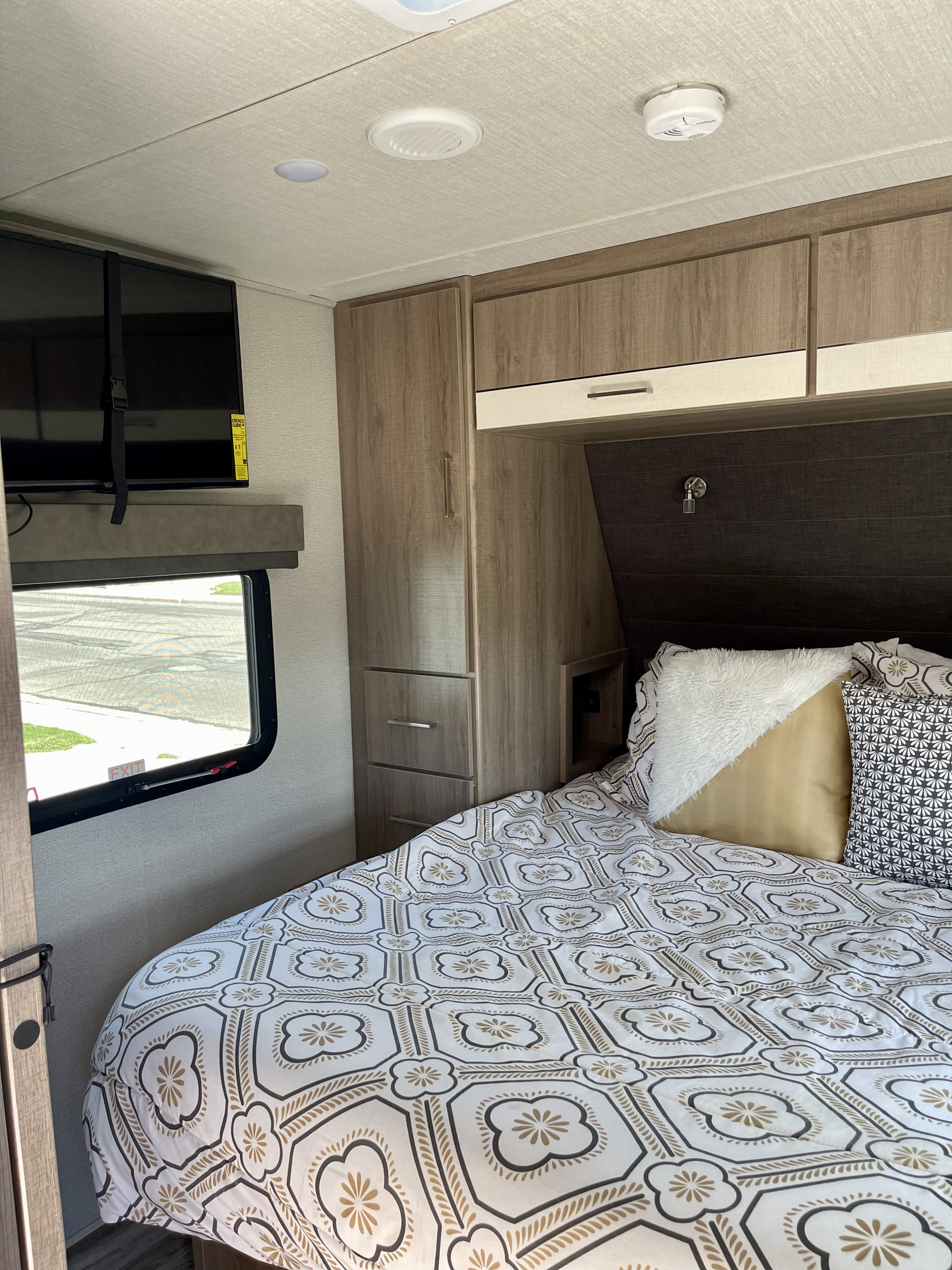Cozy RV rental bedroom featuring a patterned comforter, wall-mounted TV, and ample storage for comfortable compact living.. Grand Design Imagine XLS 2021