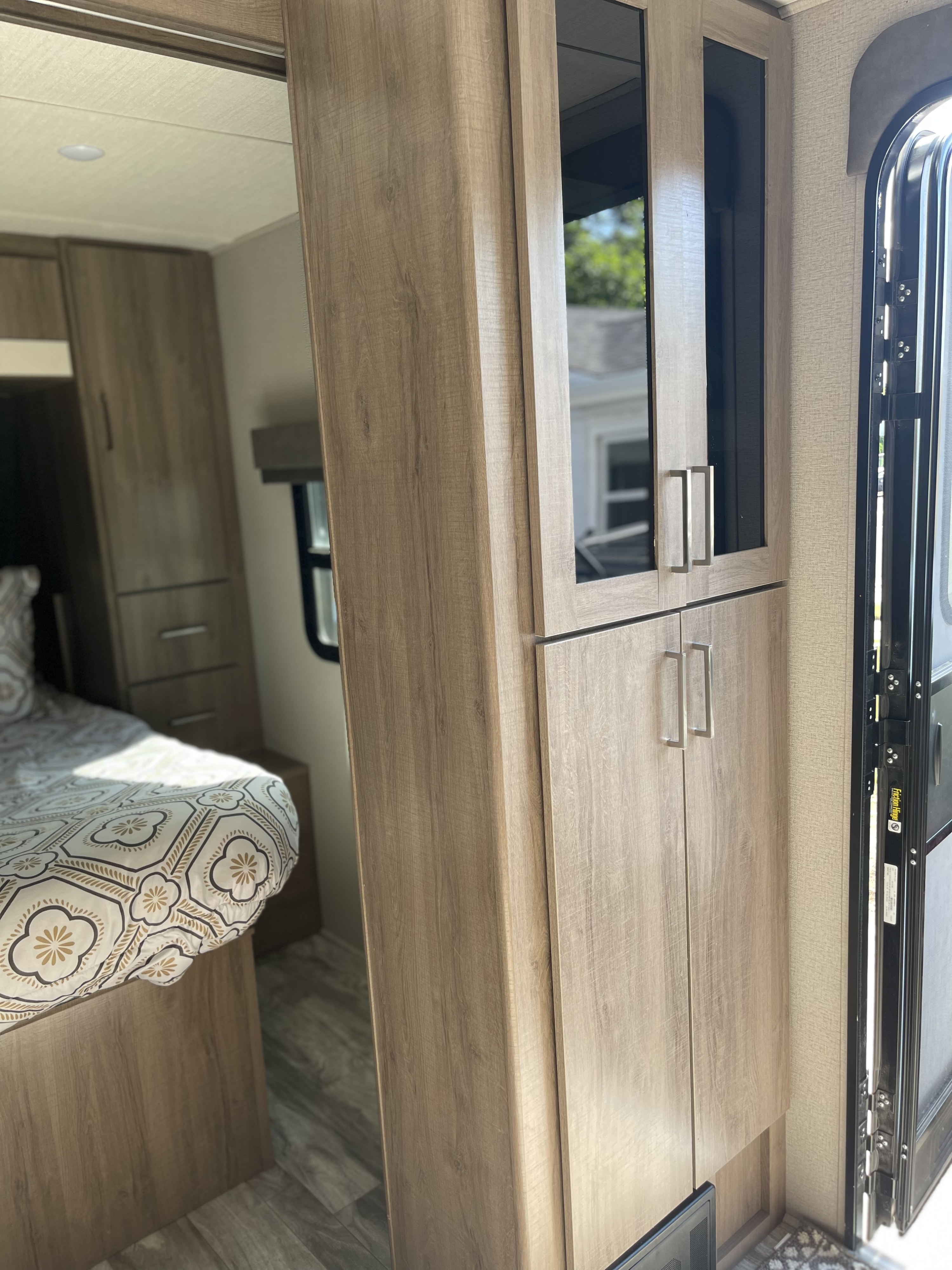 Inviting RV rental interior: cozy bedroom, light wood storage cabinets, and an open door to the outside. Your perfect camper escape.. Grand Design Imagine XLS 2021