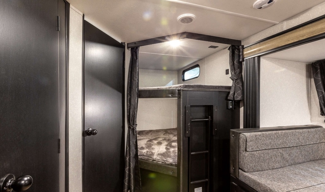 RV rental interior featuring comfortable bunk beds with a built-in ladder, privacy curtains, and a cozy sofa.. Forest River Cherokee Grey Wolf 2022