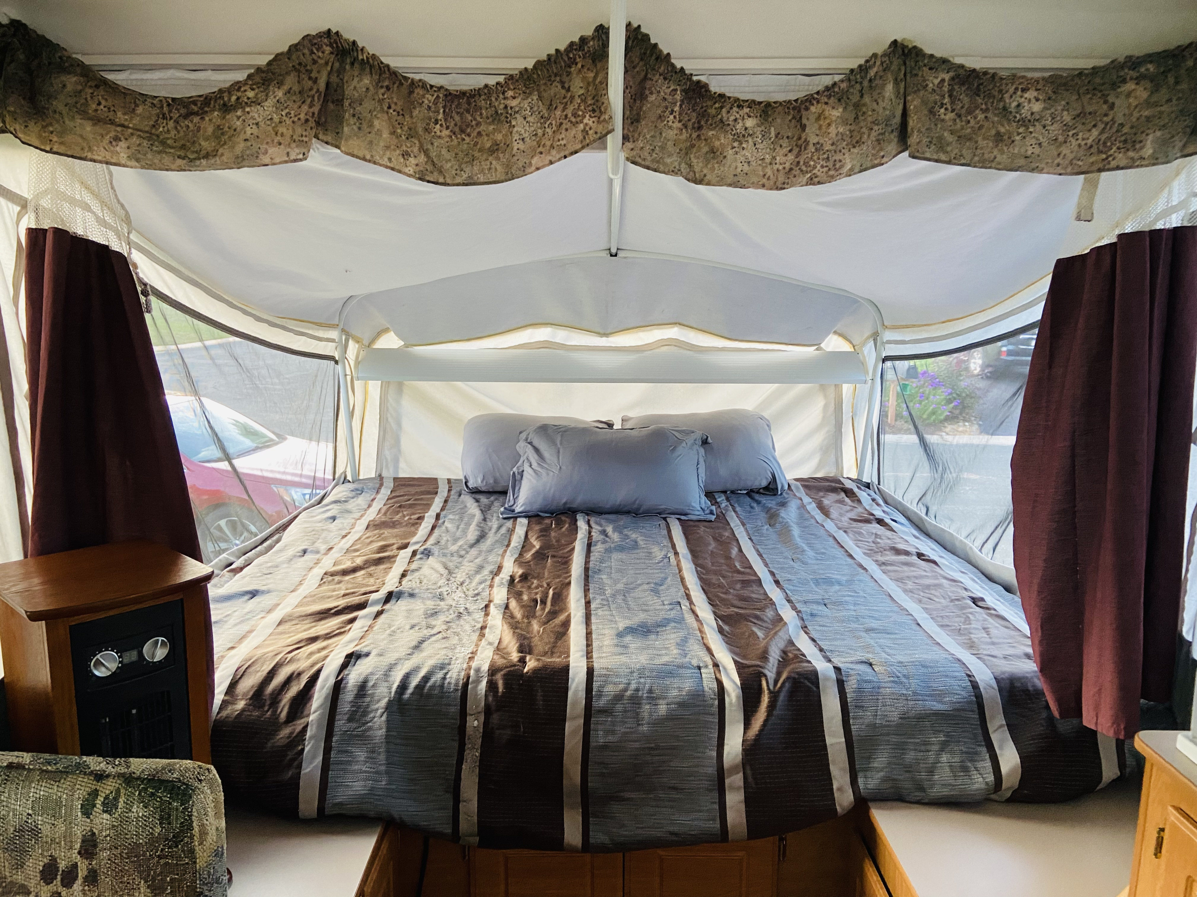Cozy pop-up RV rental interior: large bed with striped bedding, grey pillows, and patterned valances.. Coleman Americana Bayside 2002