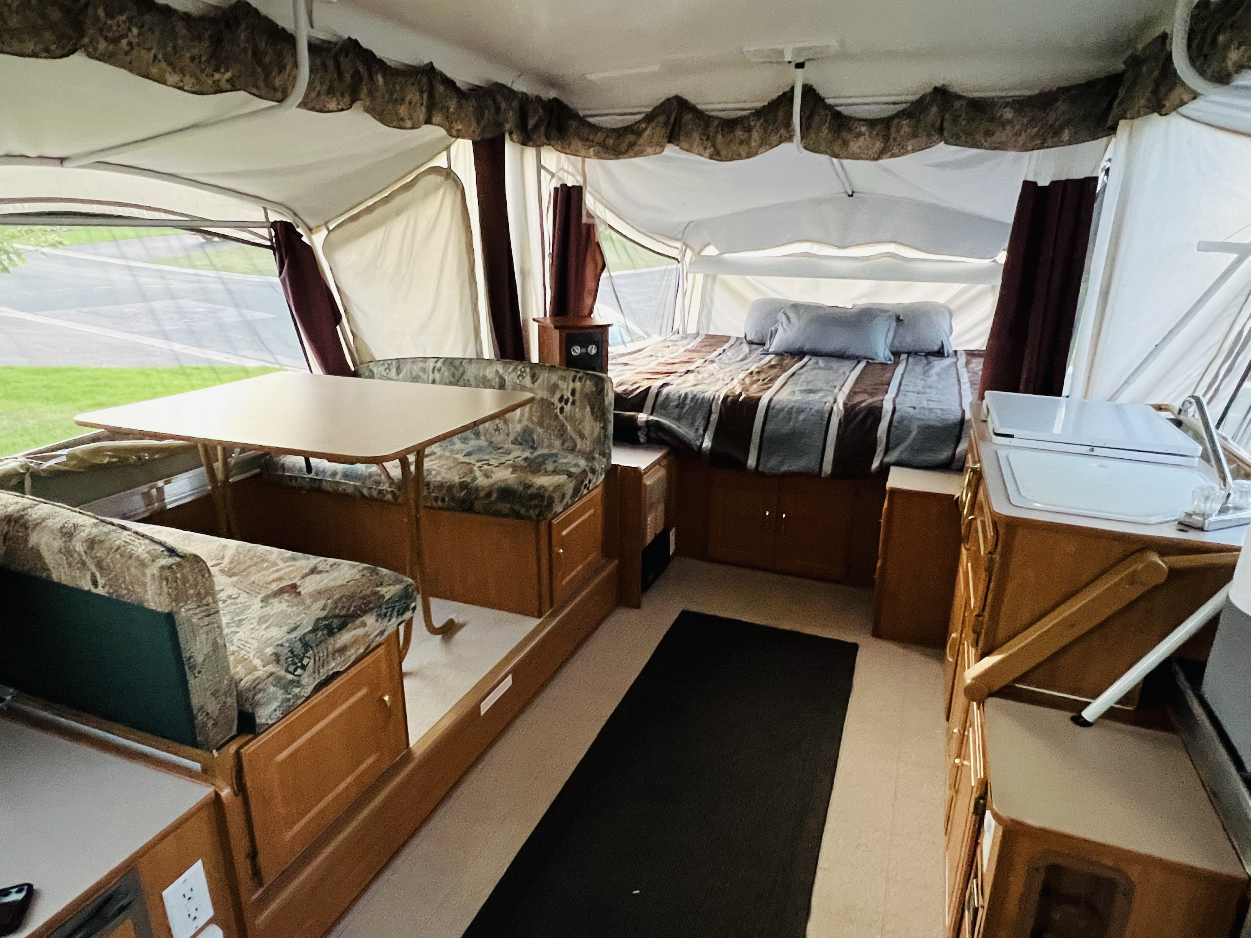 Spacious pop-up camper RV rental interior features a dinette, large bed, and kitchen, offering comfortable travel living.. Coleman Americana Bayside 2002