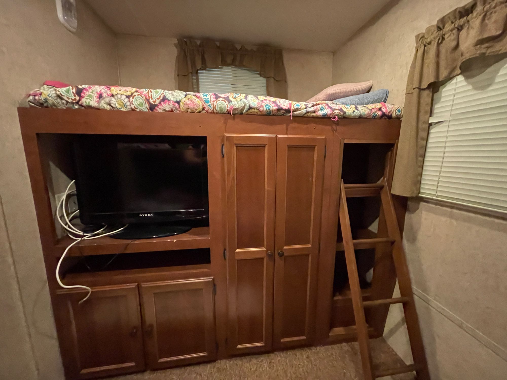 This RV rental features a cozy bunk bed with colorful bedding, a TV unit, built-in storage cabinets, and a ladder.. Heartland Prowler 2012