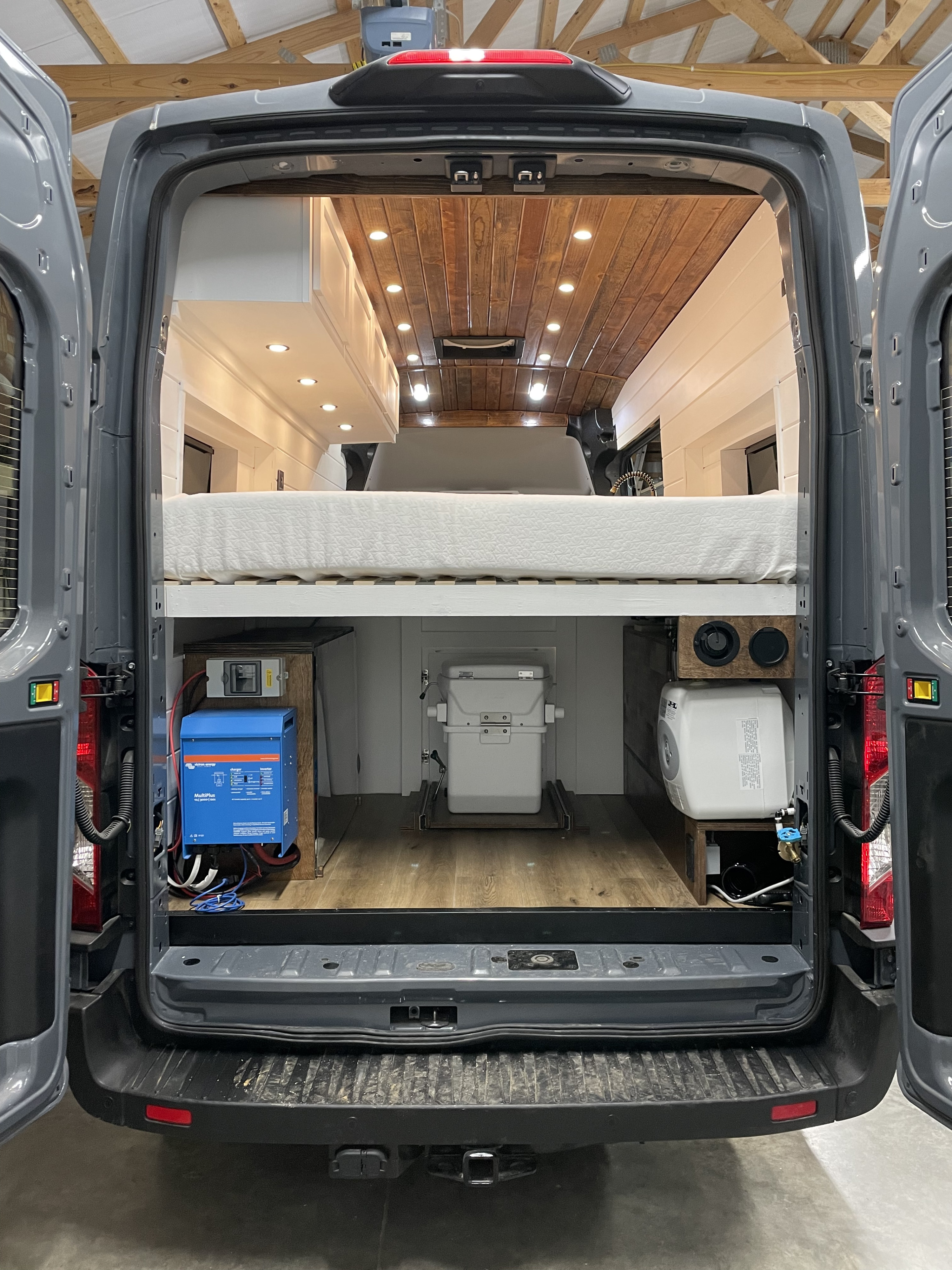 Inside this custom gray camper van RV rental: a comfortable bed, Victron power system, slide-out toilet, and water heater.. Ford Transit 2021